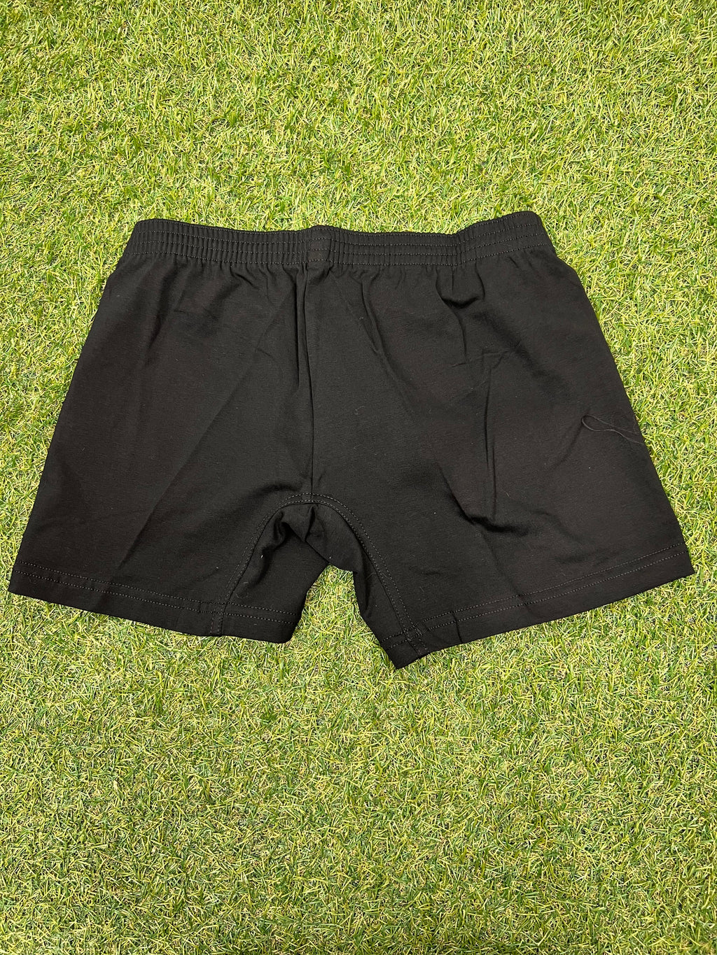 Back view of black women’s volleyball shorts showing elastic waistband and plain design on green grass