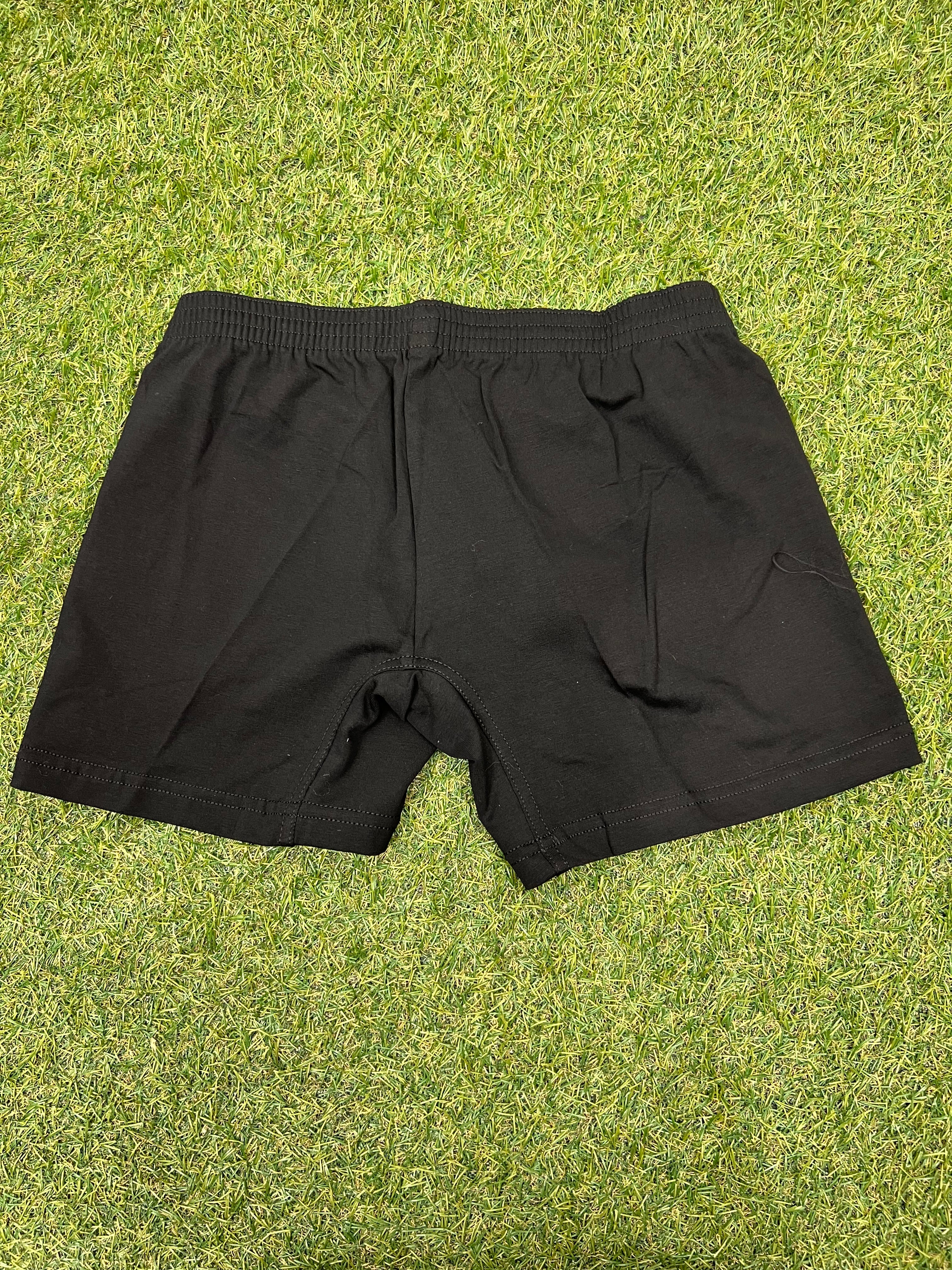 Back view of black women’s volleyball shorts showing elastic waistband and plain design on green grass