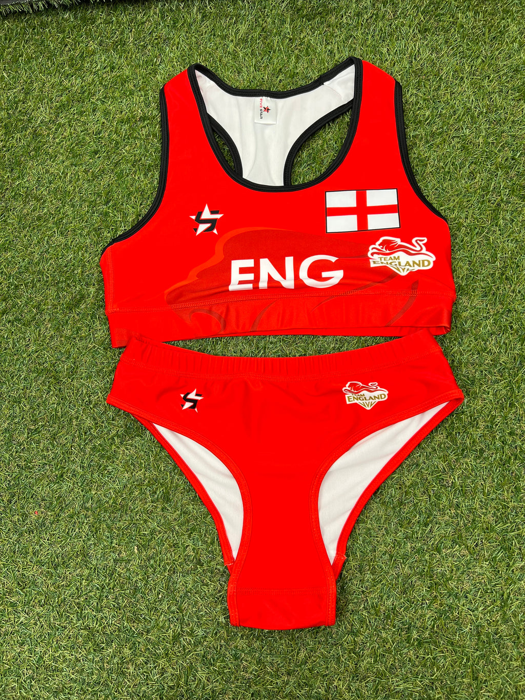 Front view of Women's Team England red volleyball bikini set laid on grass