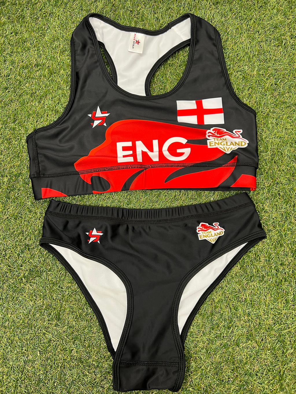 Front view of women's black Team England beach volleyball bikini top and bottoms laid flat on grass