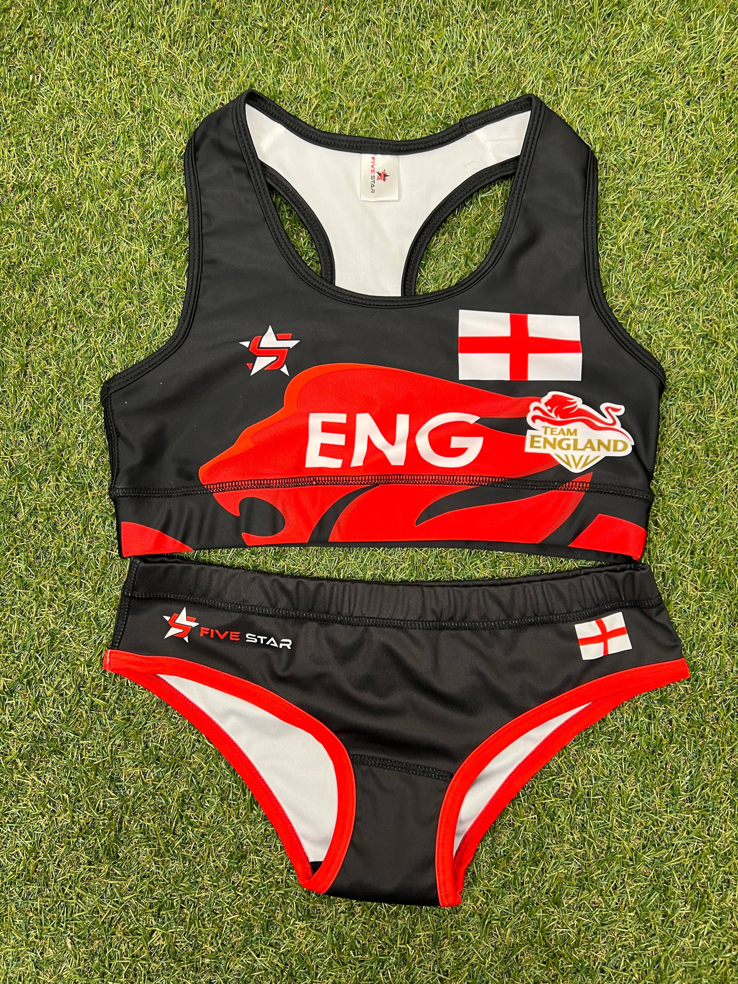 Front view of women’s Team England black and red beach volleyball bikini laid out on grass