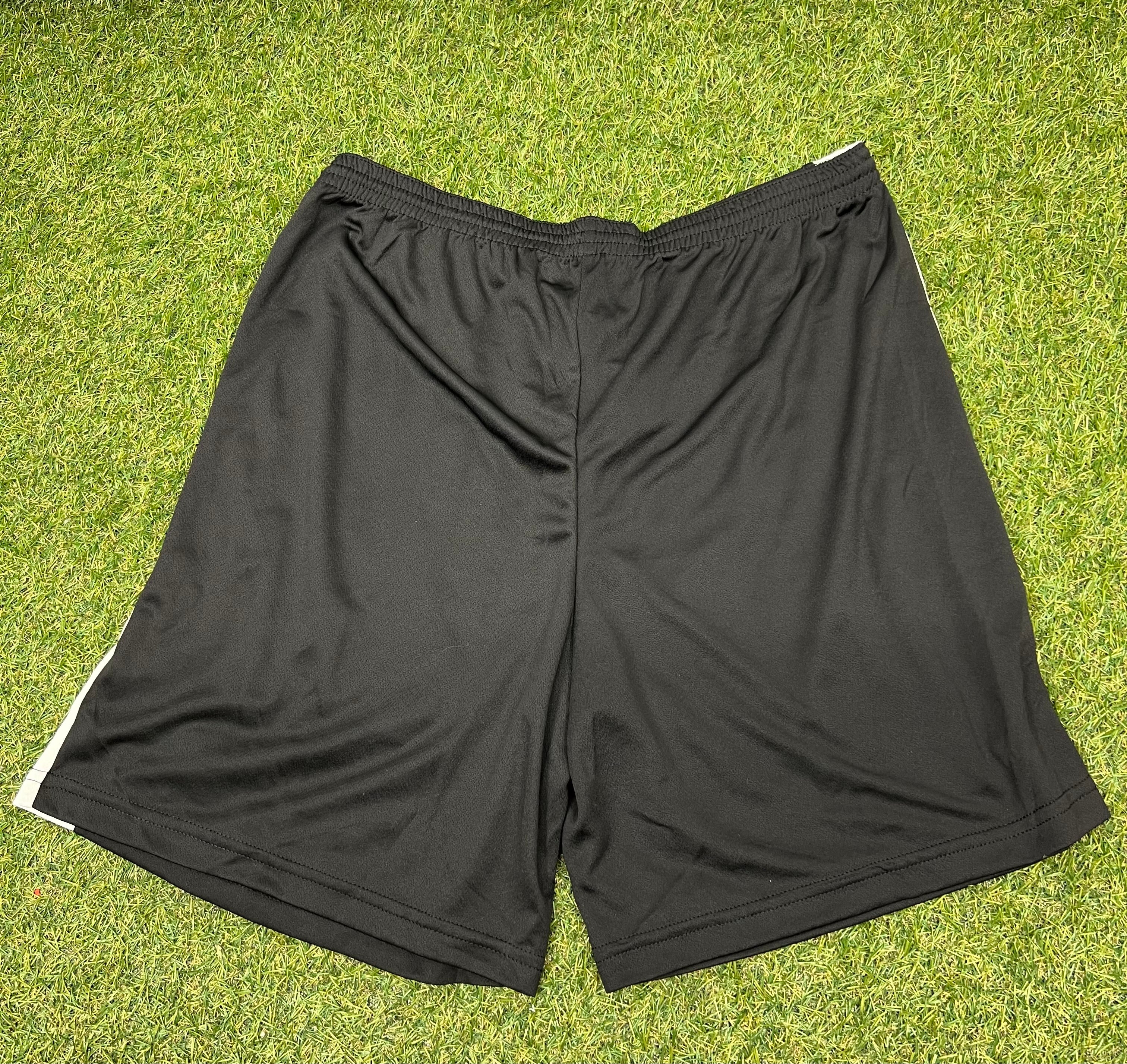 Back view of black men’s volleyball shorts with white side panels on grass background