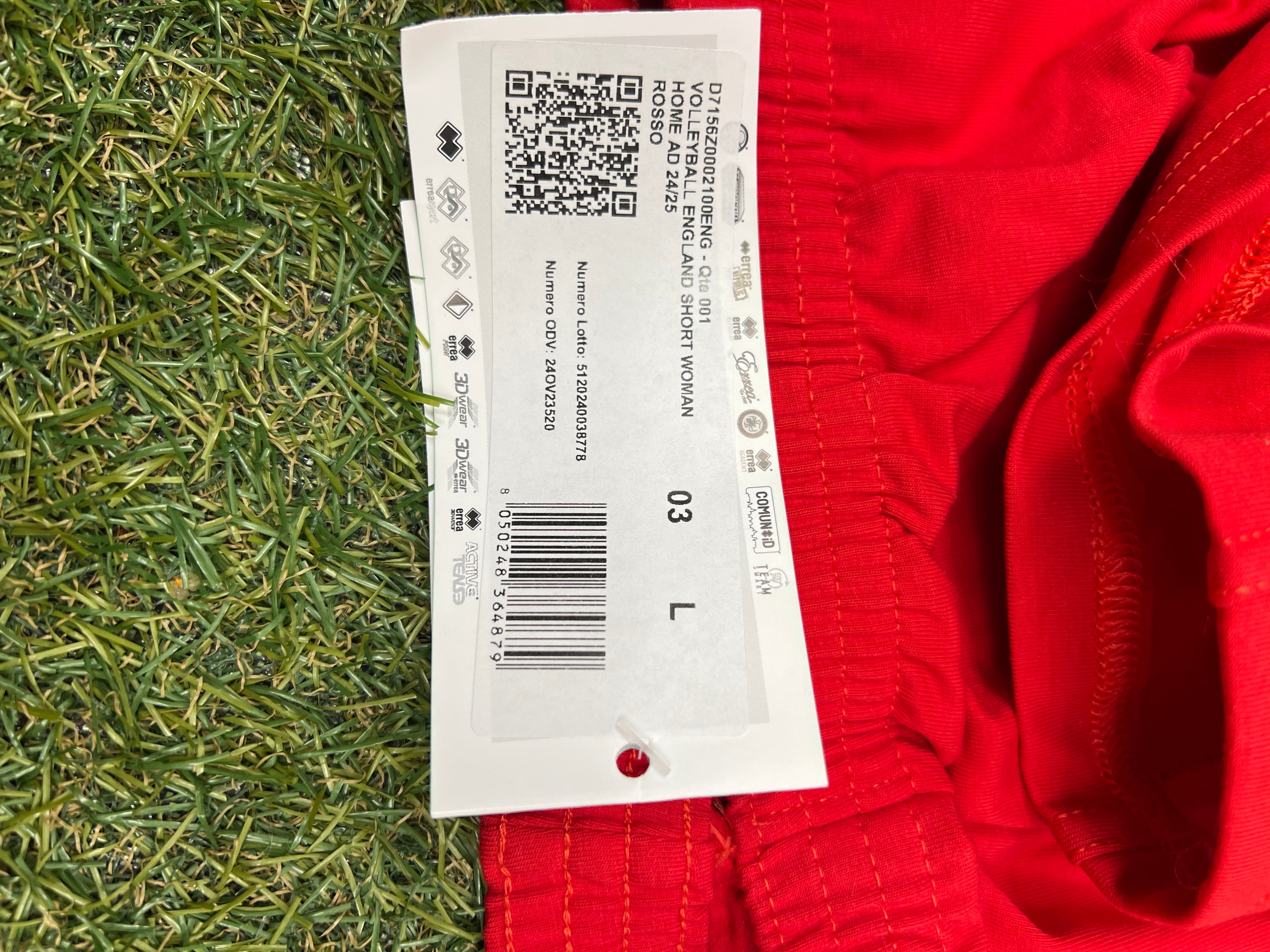 Close-up of size L tag showing product details including 'Volleyball England short woman' and barcode on red shorts