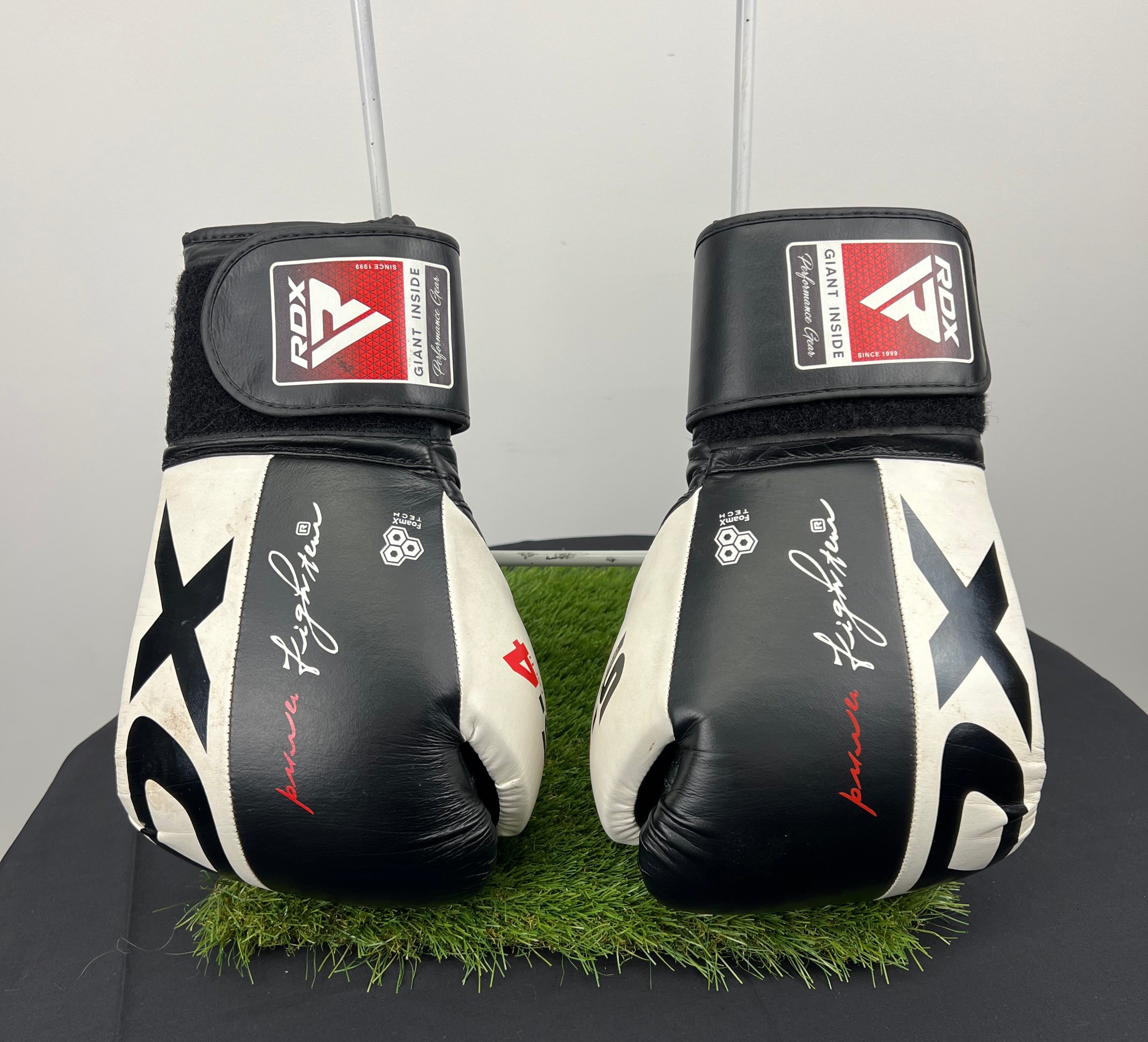 Front view of RDX Safe-Tech 4 black and white boxing gloves on artificial grass