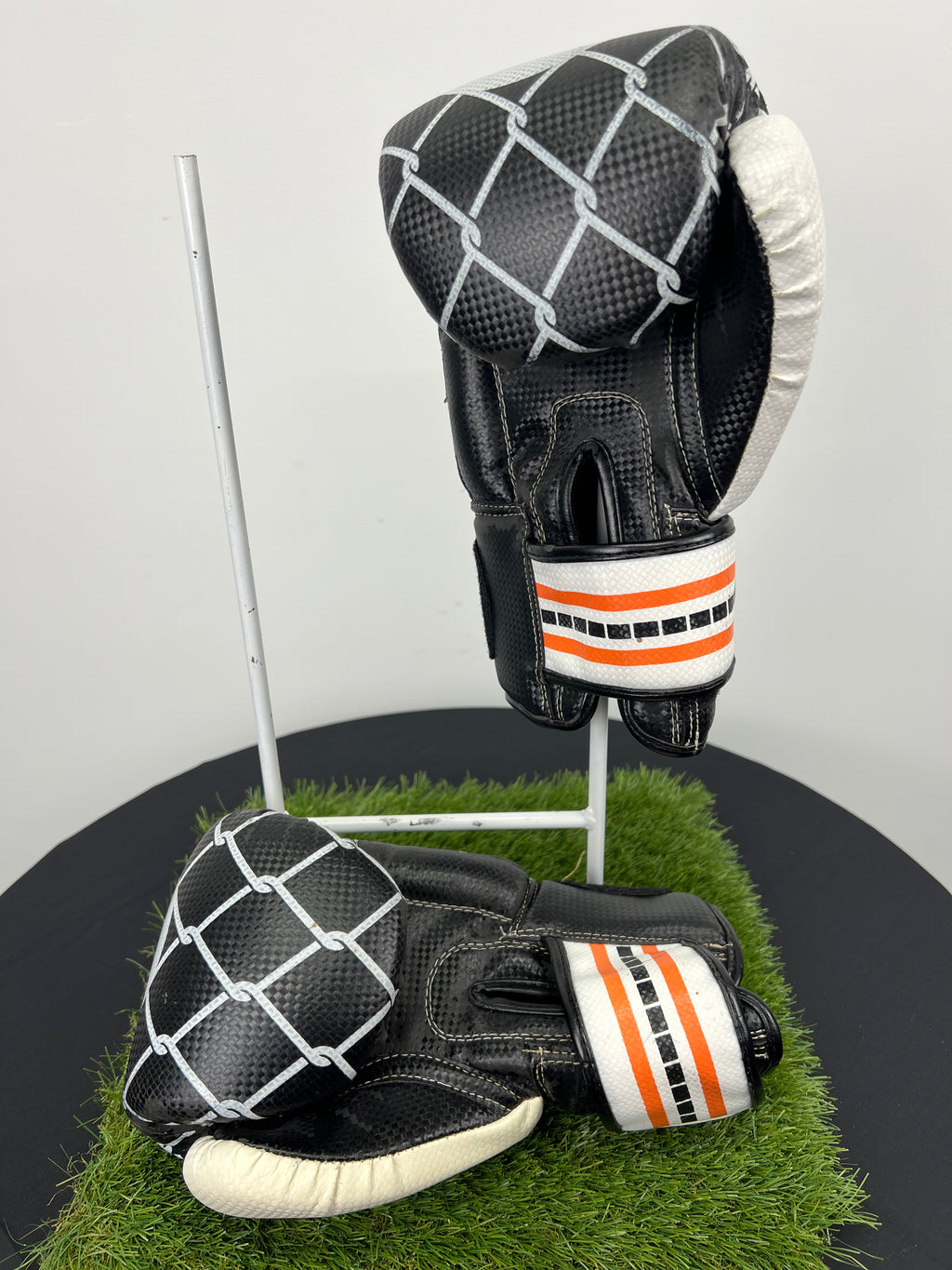 Side view of black and white Sport EQ boxing gloves with adjustable wrist straps displayed on grass stand