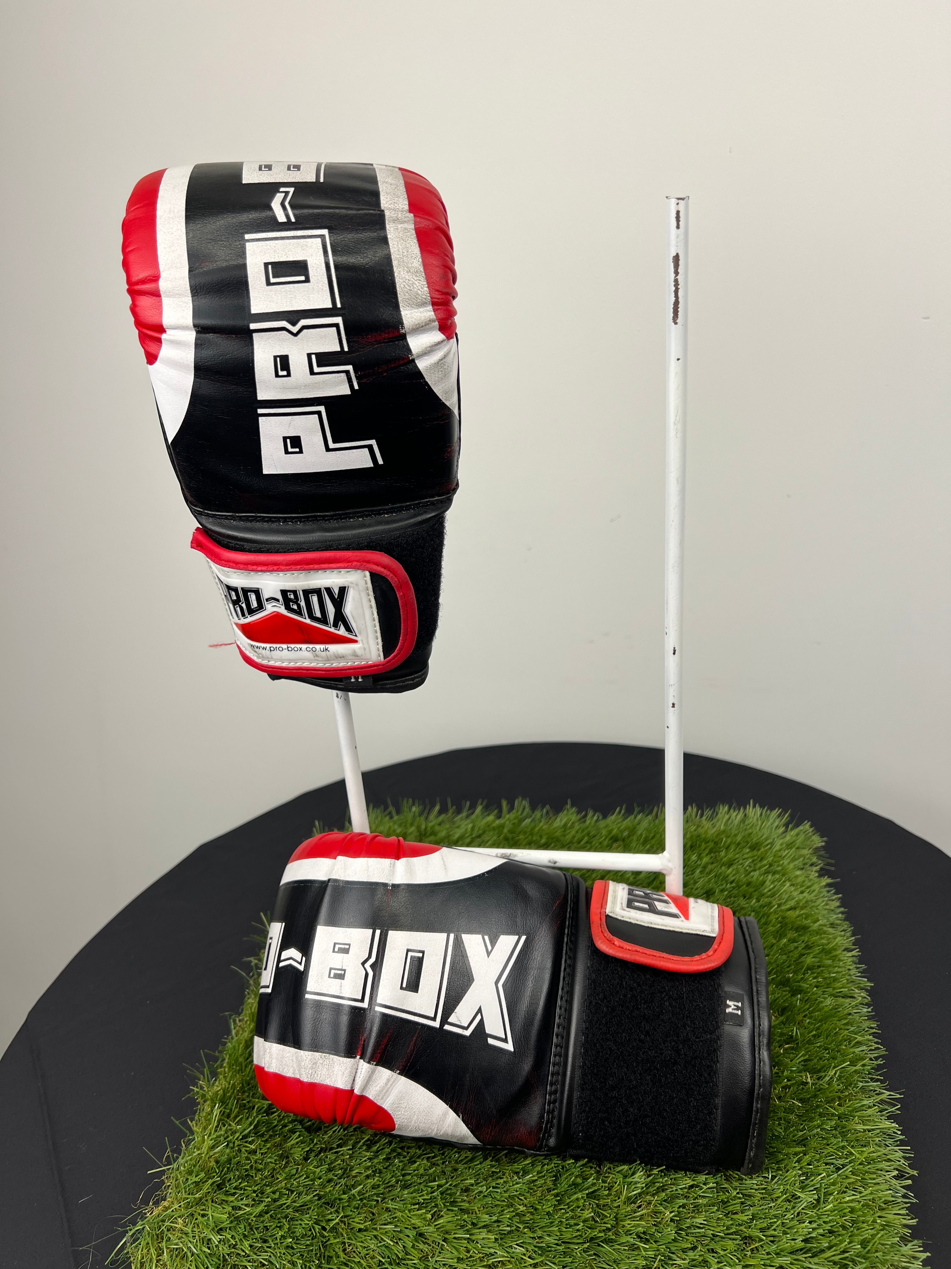 Side and top view of one Pro Box boxing glove with visible velcro strap and branding on black and red synthetic material