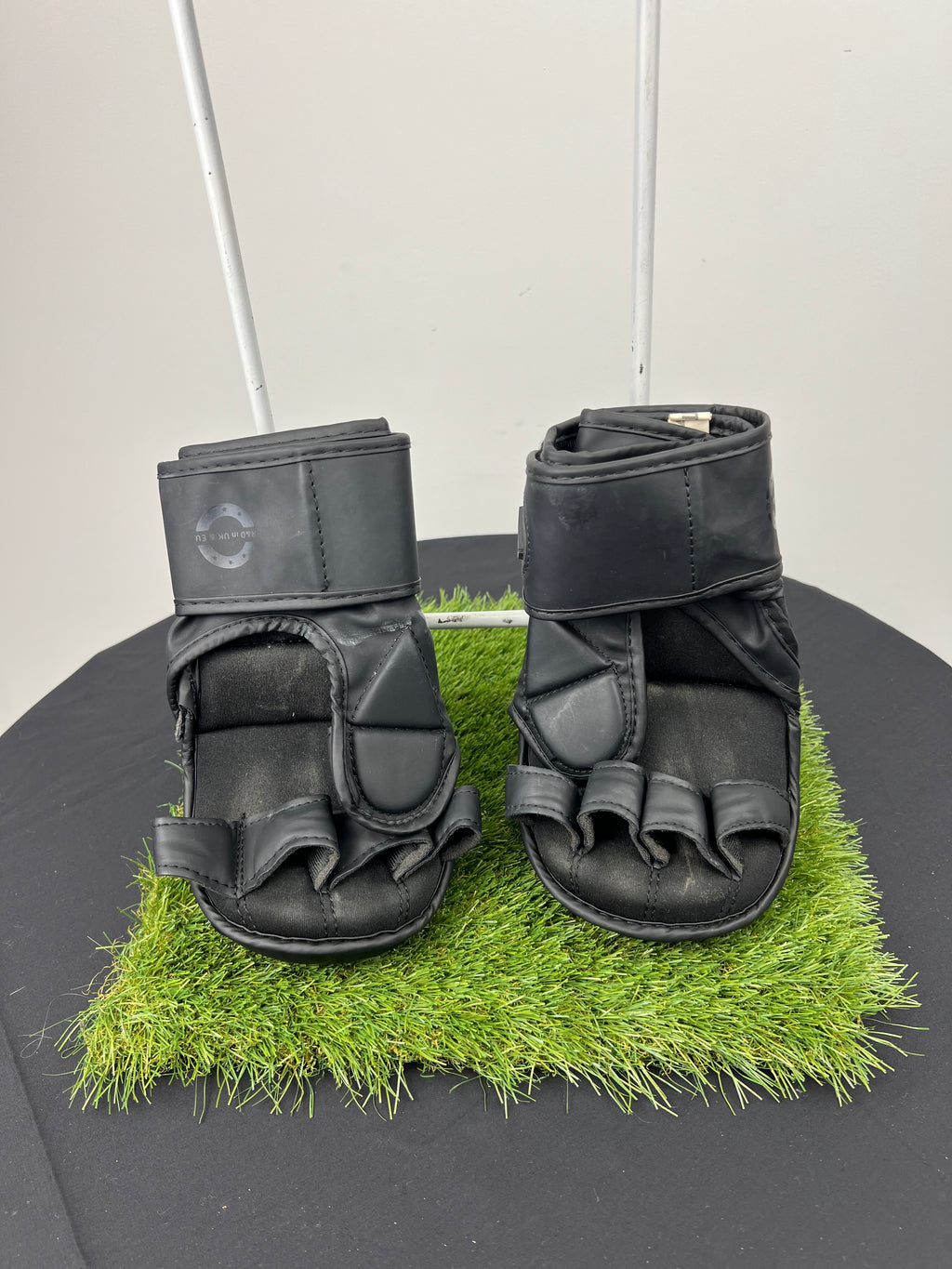 Back view of Kara by RDX 7oz black grappling gloves showing finger loops and adjustable wrist strap on artificial grass