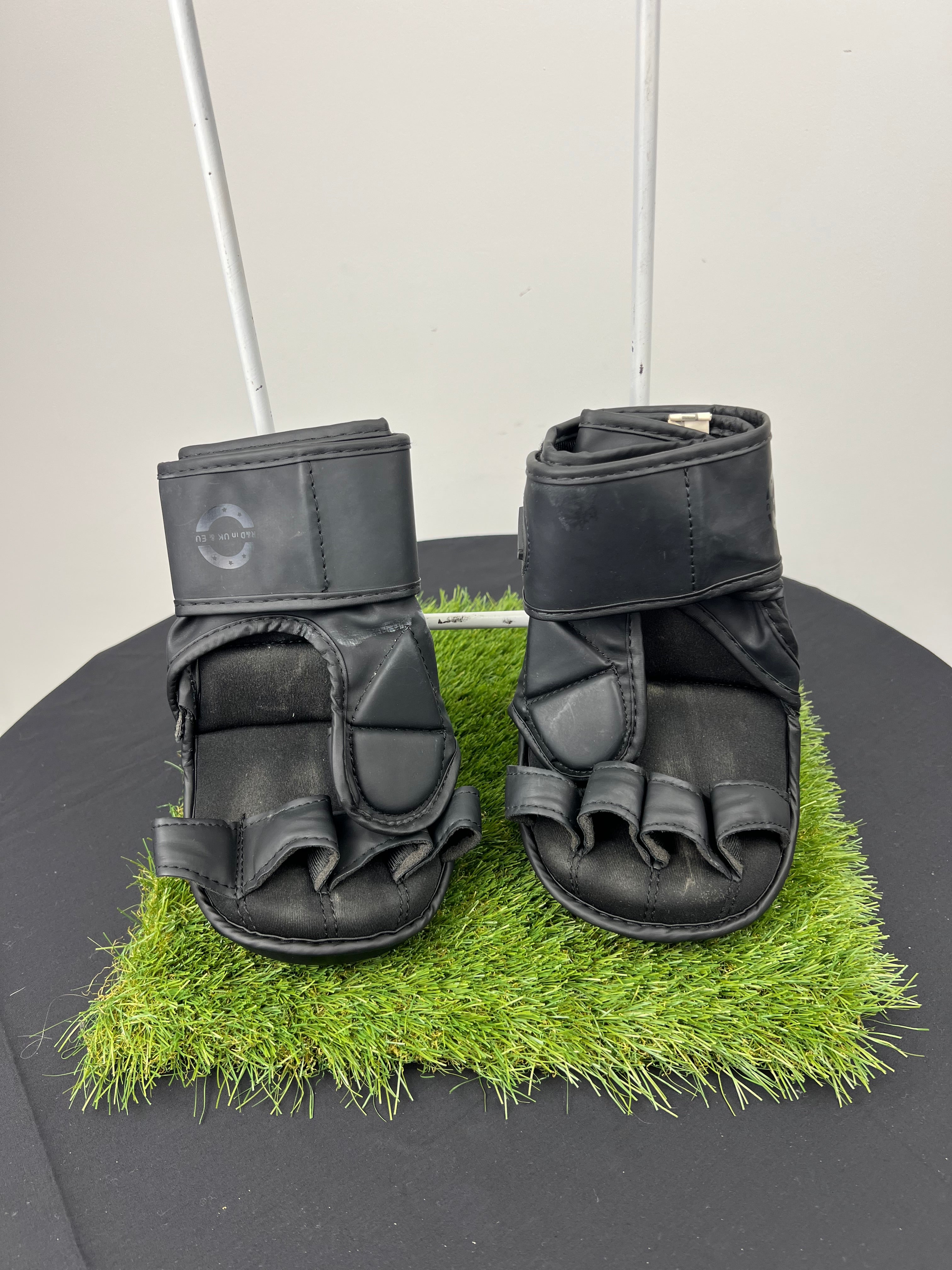 Back view of Kara by RDX 7oz black grappling gloves showing finger loops and adjustable wrist strap on artificial grass