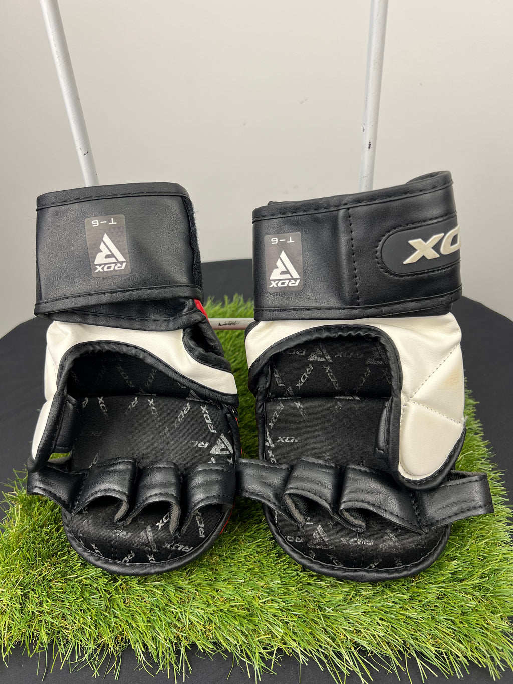 Back view of red and black RDX T6 7oz grappling gloves showing open finger design and internal grip padding on artificial grass