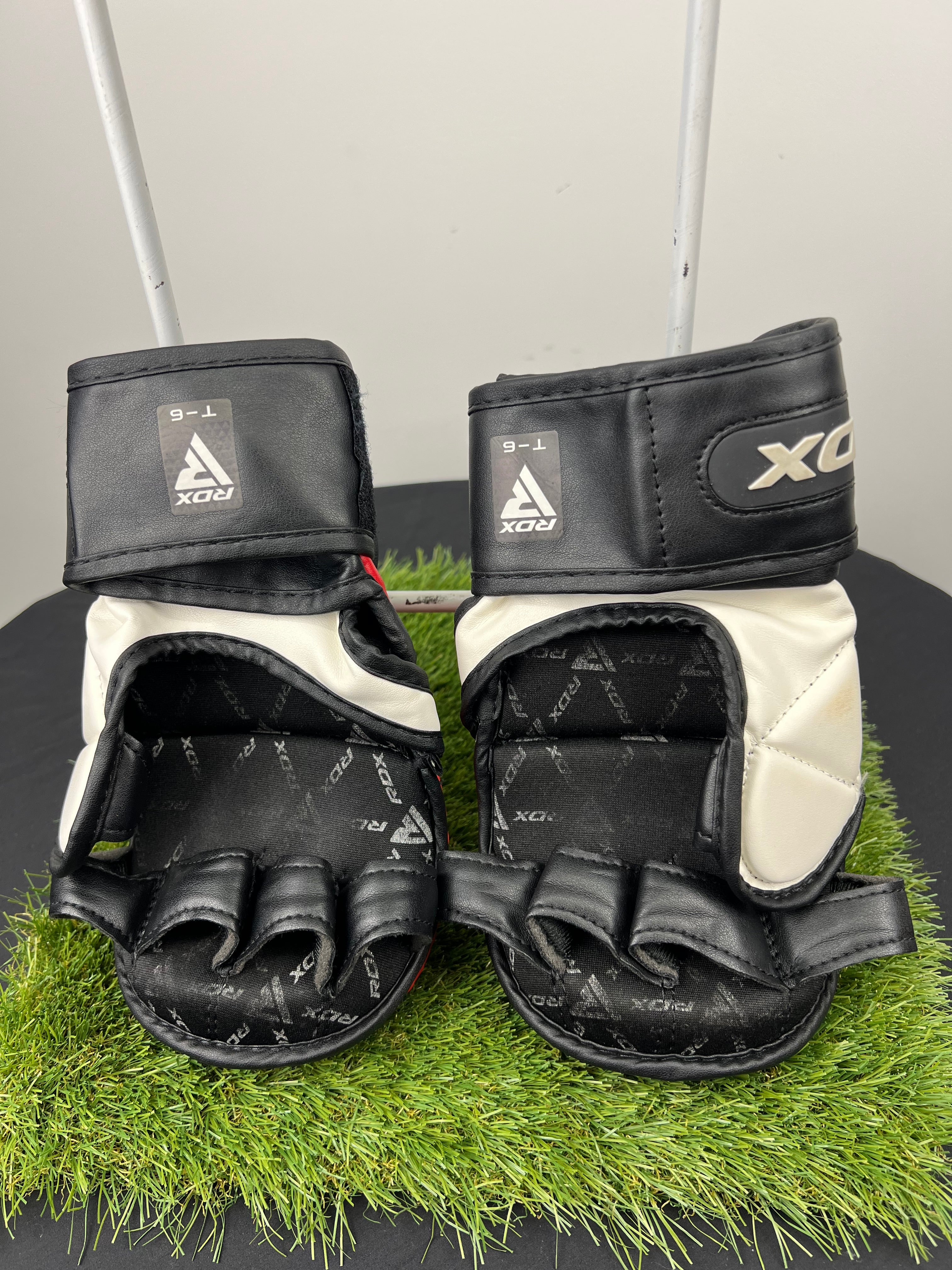 Back view of red and black RDX T6 7oz grappling gloves showing open finger design and internal grip padding on artificial grass