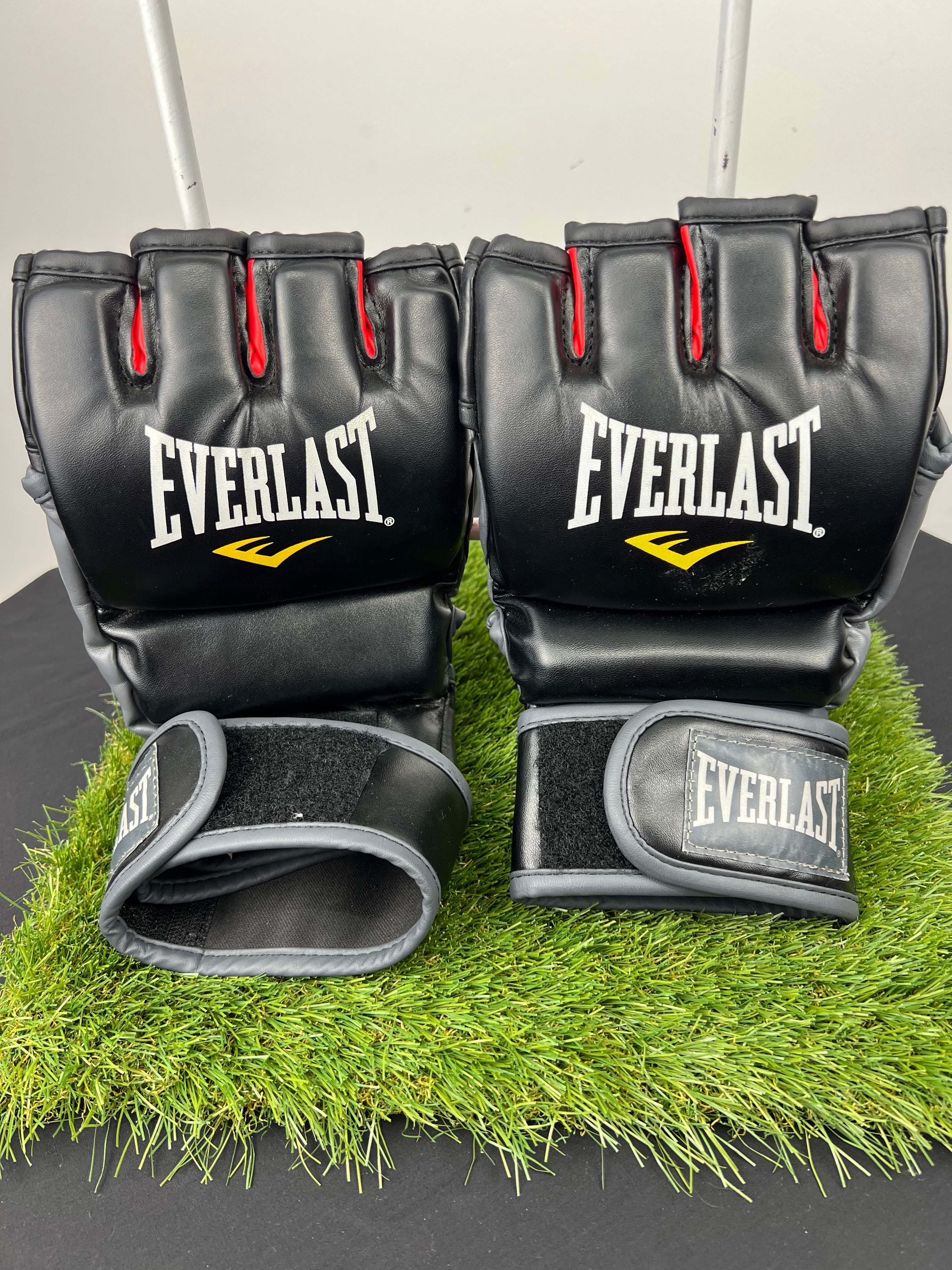 Everlast MMA grappling gloves in black with red finger accents, front view showing knuckle padding and wrist strap