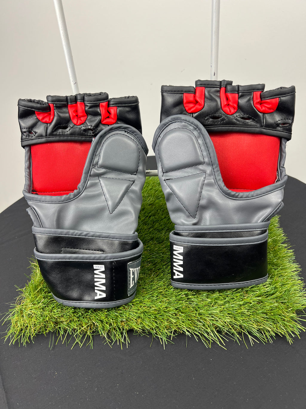 Back view of Everlast MMA gloves showing grey palm area, red finger sections, and black wrist strap with MMA branding