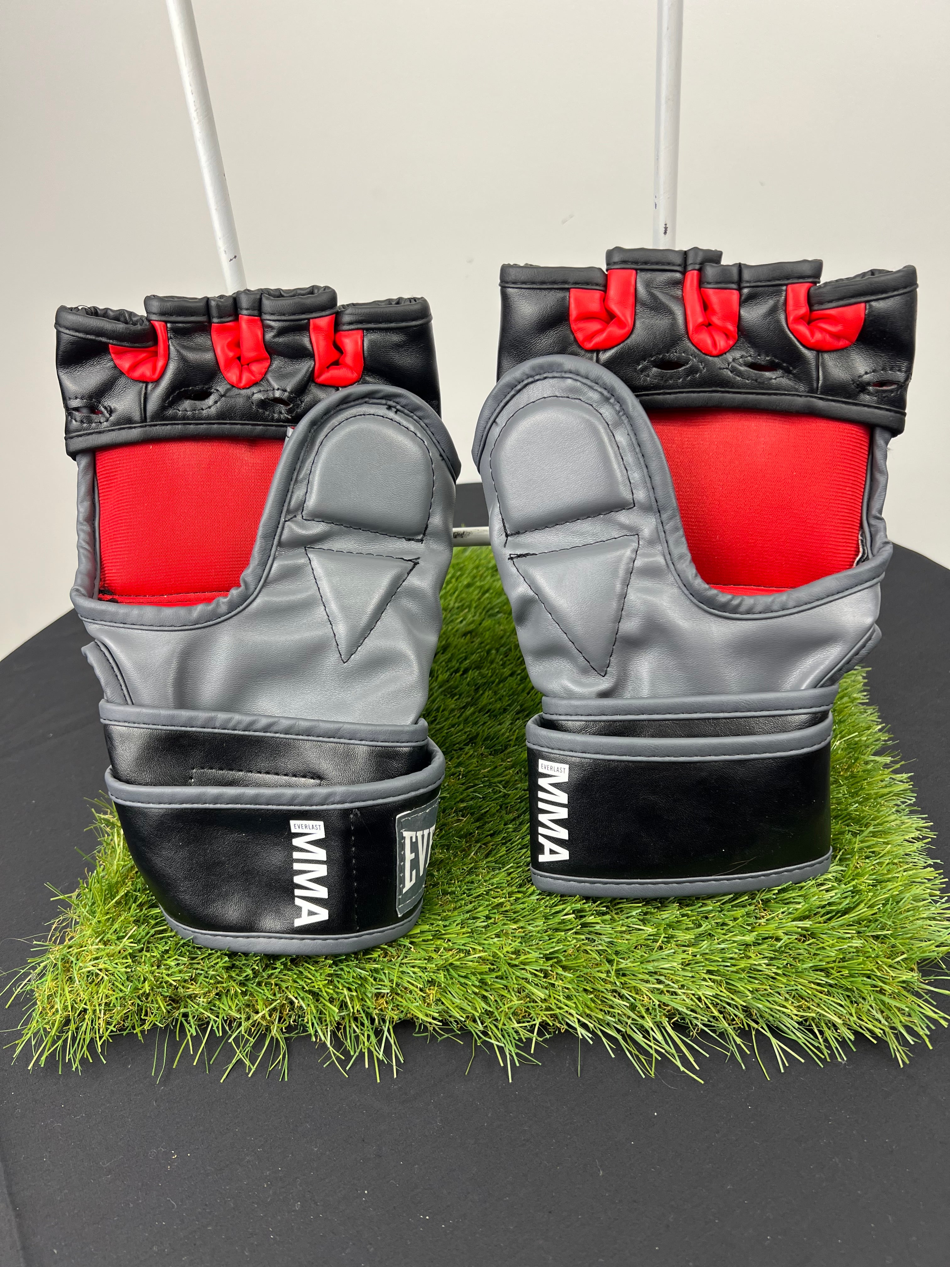 Back view of Everlast MMA gloves showing grey palm area, red finger sections, and black wrist strap with MMA branding