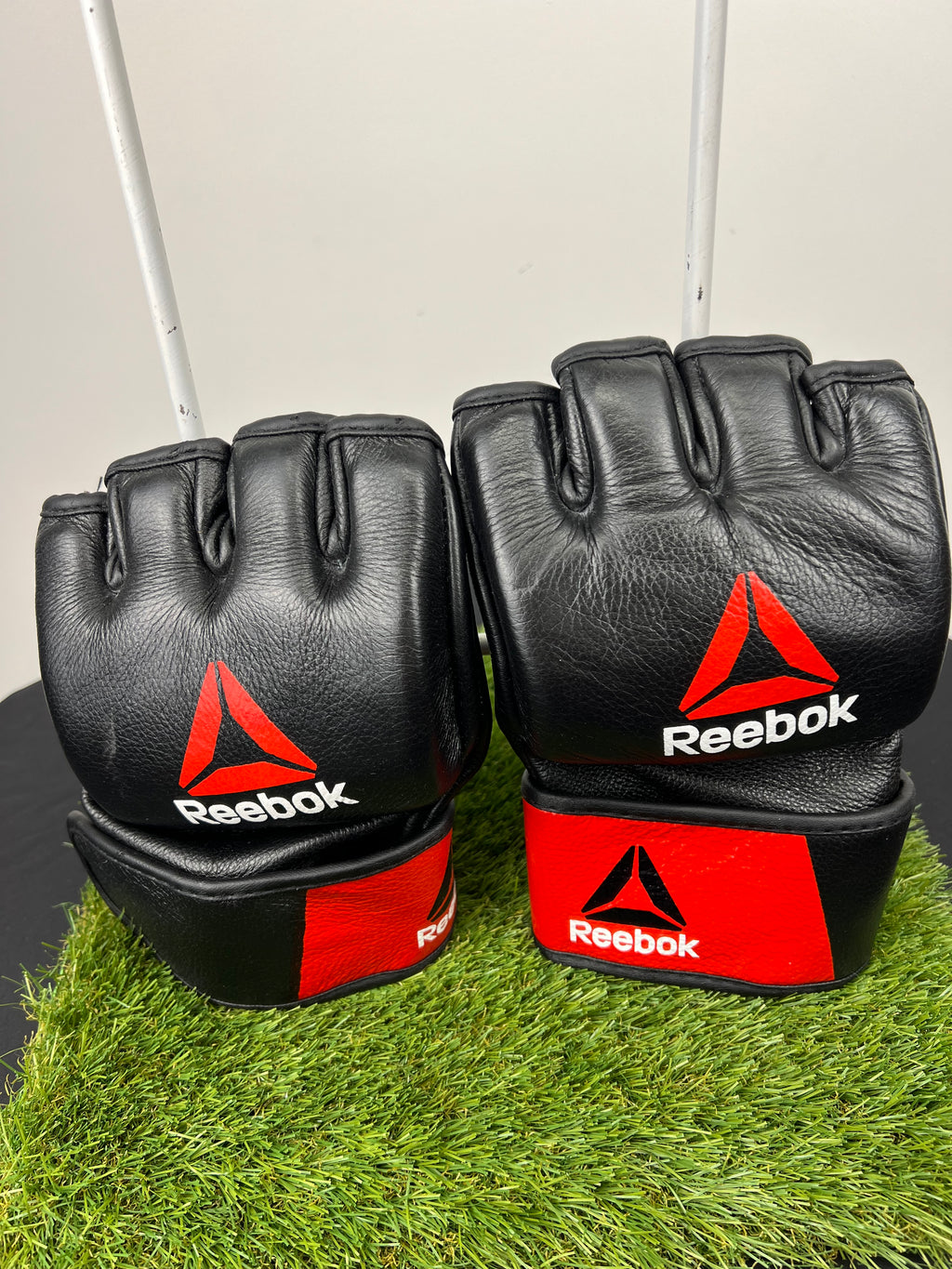 Pair of black Reebok open palm grappling gloves showing front knuckle side with red and white logos