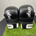 Front view of black Origin grappling gloves with white wrist straps placed on artificial grass