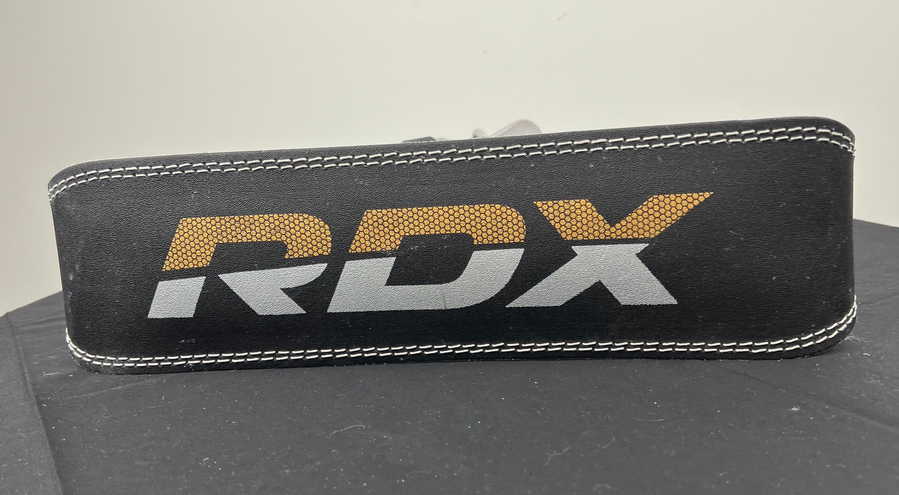 Close-up of black RDX 4 inch weightlifting belt with white stitching and RDX logo in gold and silver