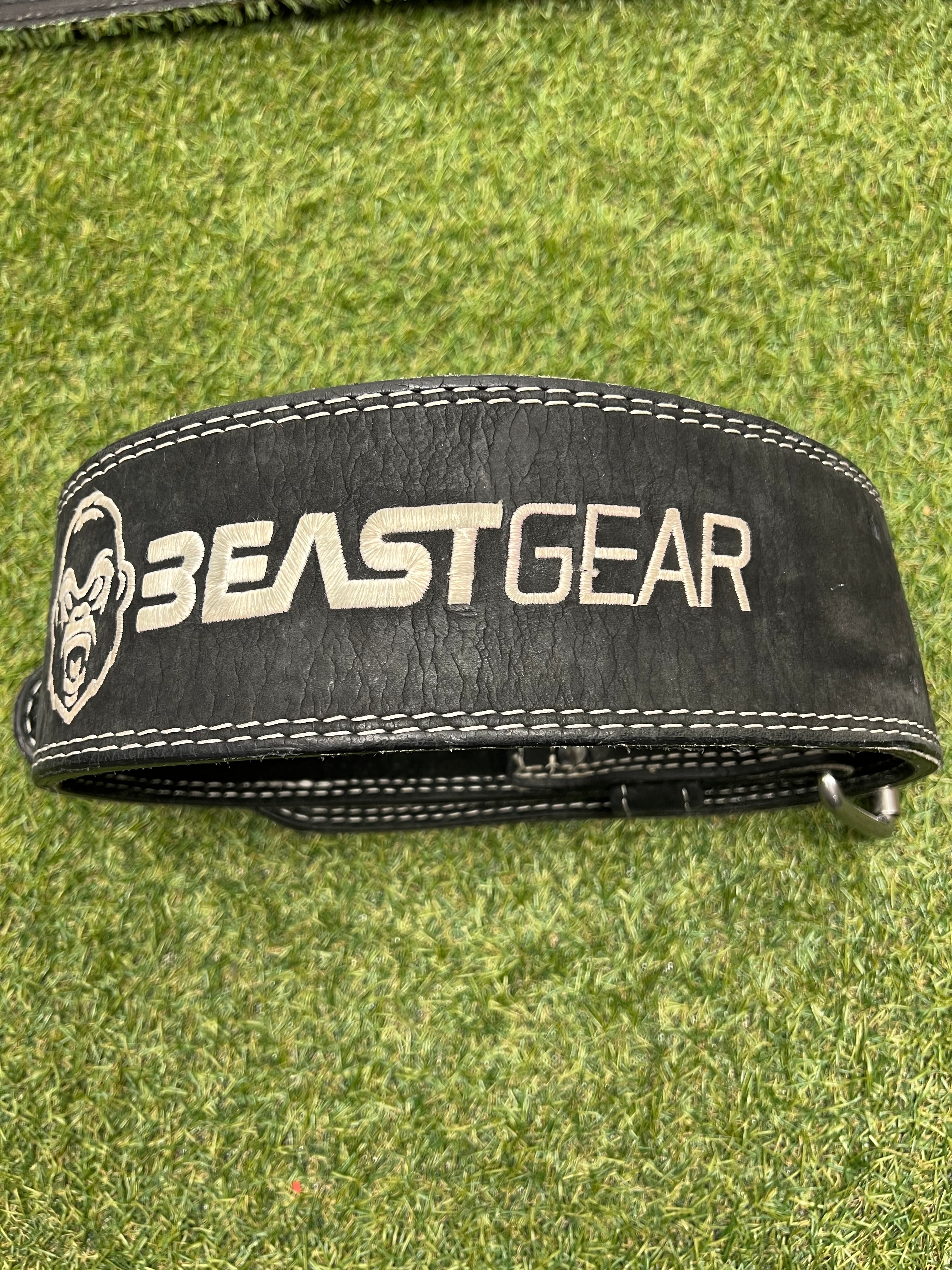 Black leather Beast Gear weightlifting belt laid flat on green turf showing the front with logo and white stitching
