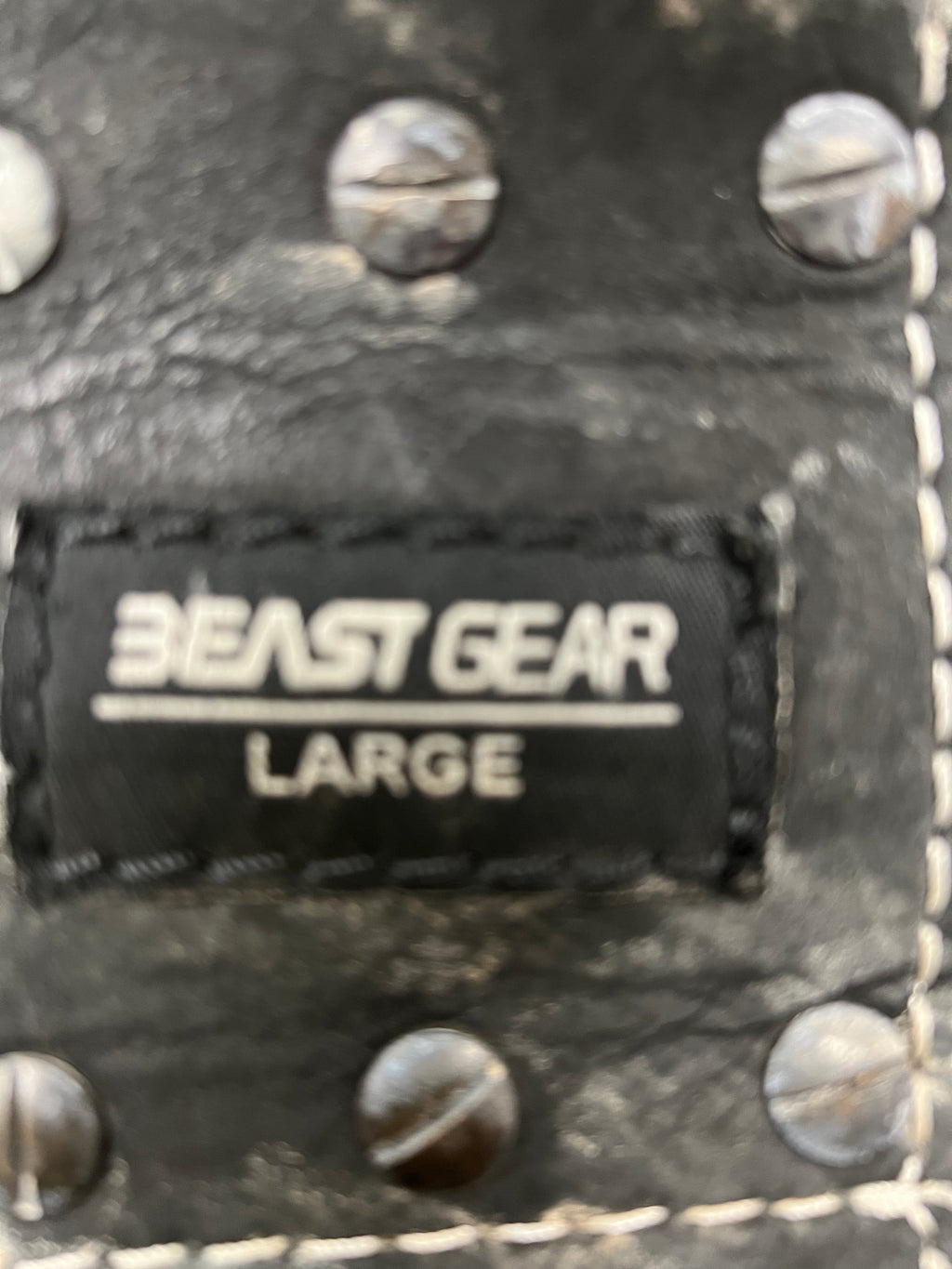 Focused view of the Beast Gear size label stitched into the black leather weightlifting belt with metal rivets