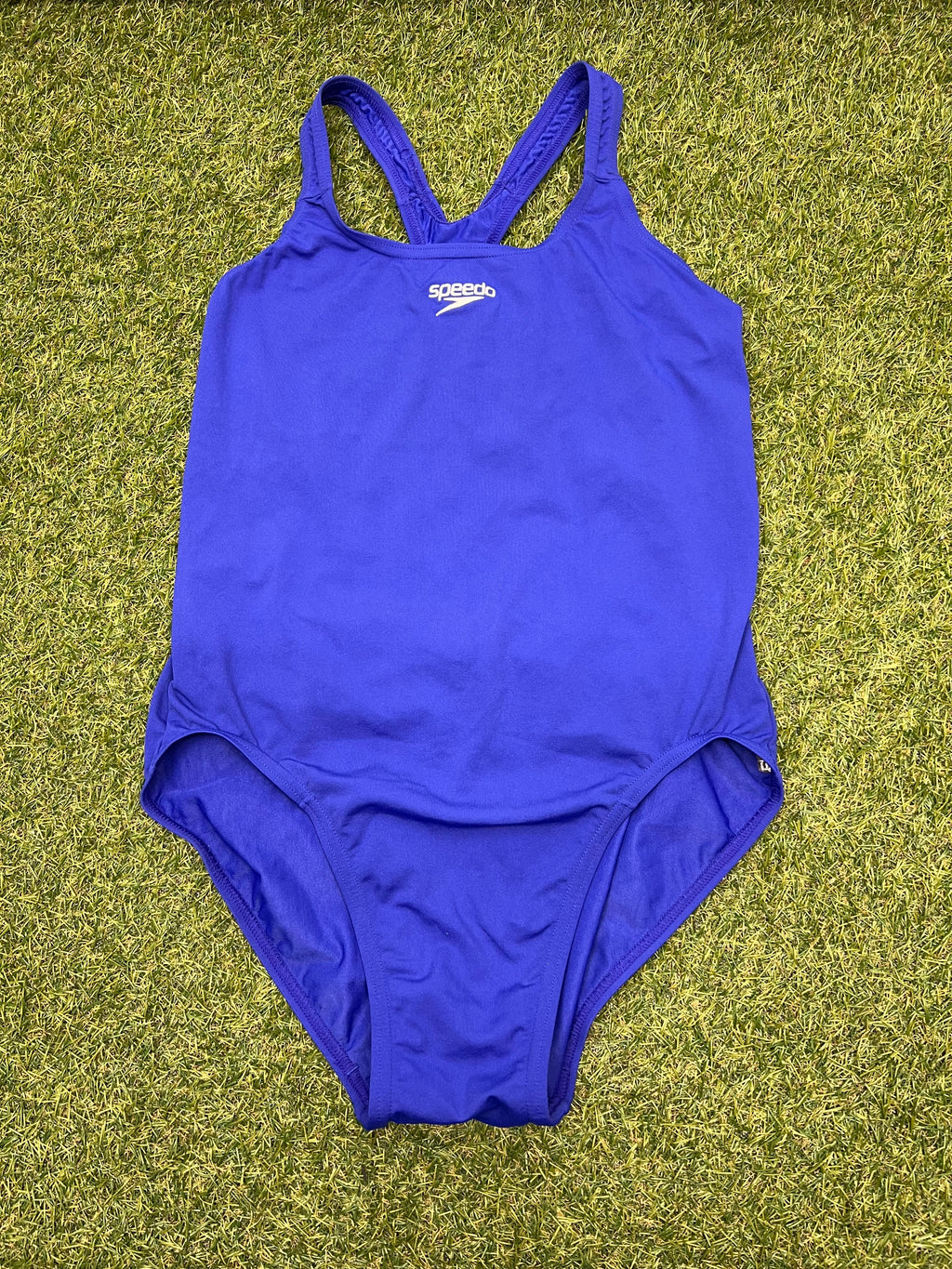 Front view of purple Speedo one-piece swimsuit laid on grass
