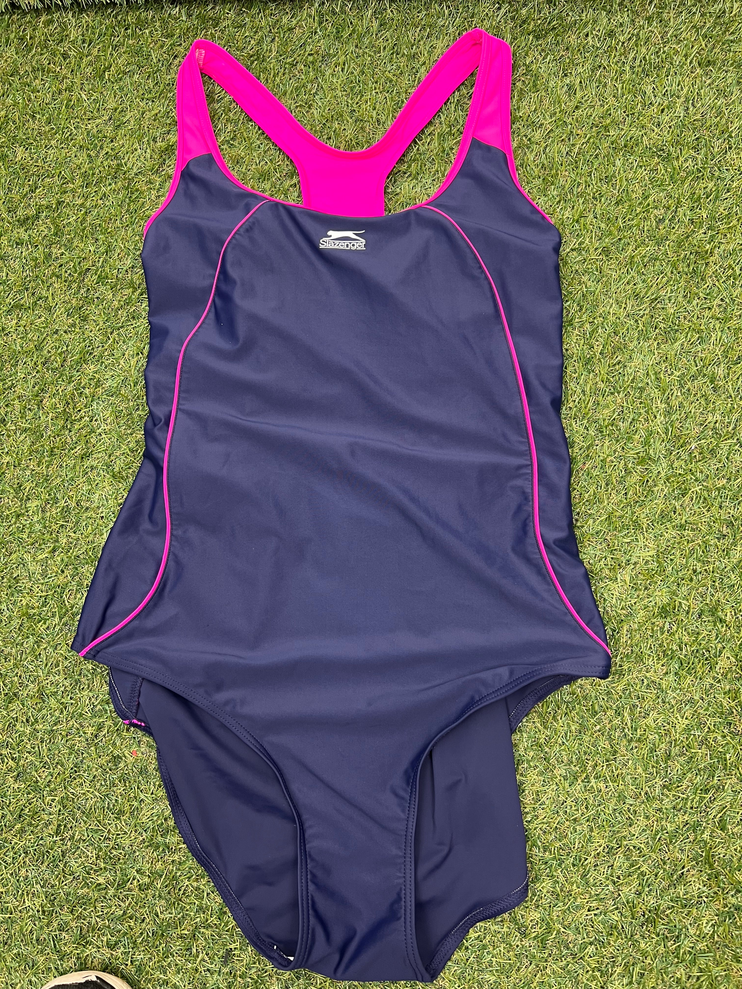 Front view of women's Slazenger racer back swimsuit in purple with pink straps and piping, laid flat on grass