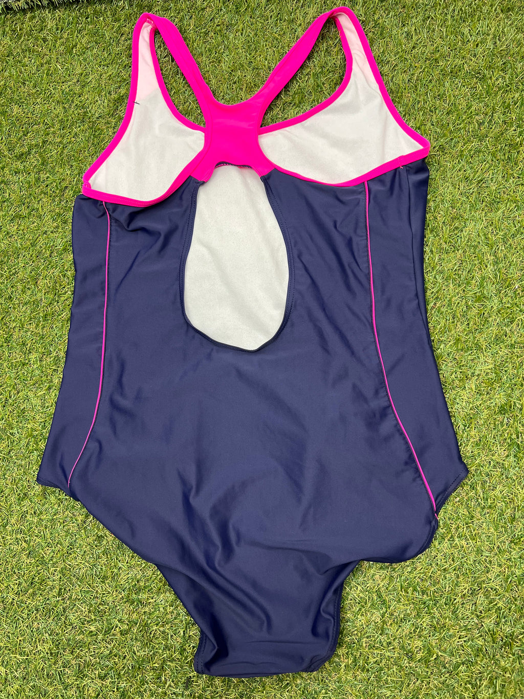 Back view of women's Slazenger racer back swimsuit showing open back design and pink trim, laid flat on grass