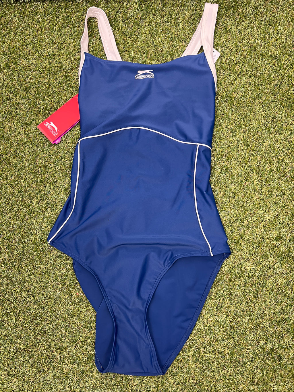 Front view of Women’s Slazenger blue swimsuit size 16 with cream straps laid on grass
