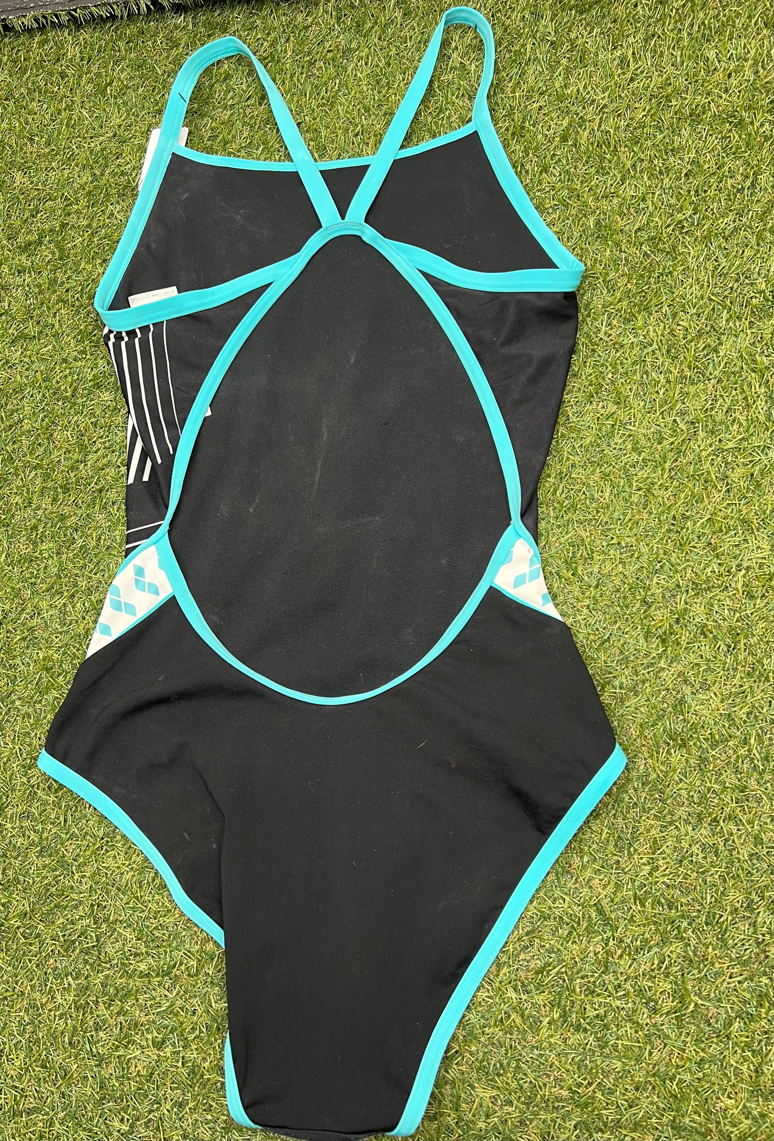 Back view of women’s black arena swimsuit showing crossed straps and open back design on grass