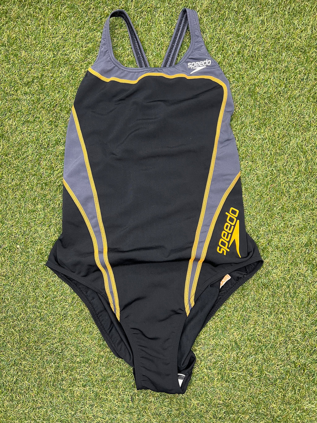 Front view of black and grey Speedo women's swimsuit with yellow detailing laid on grass
