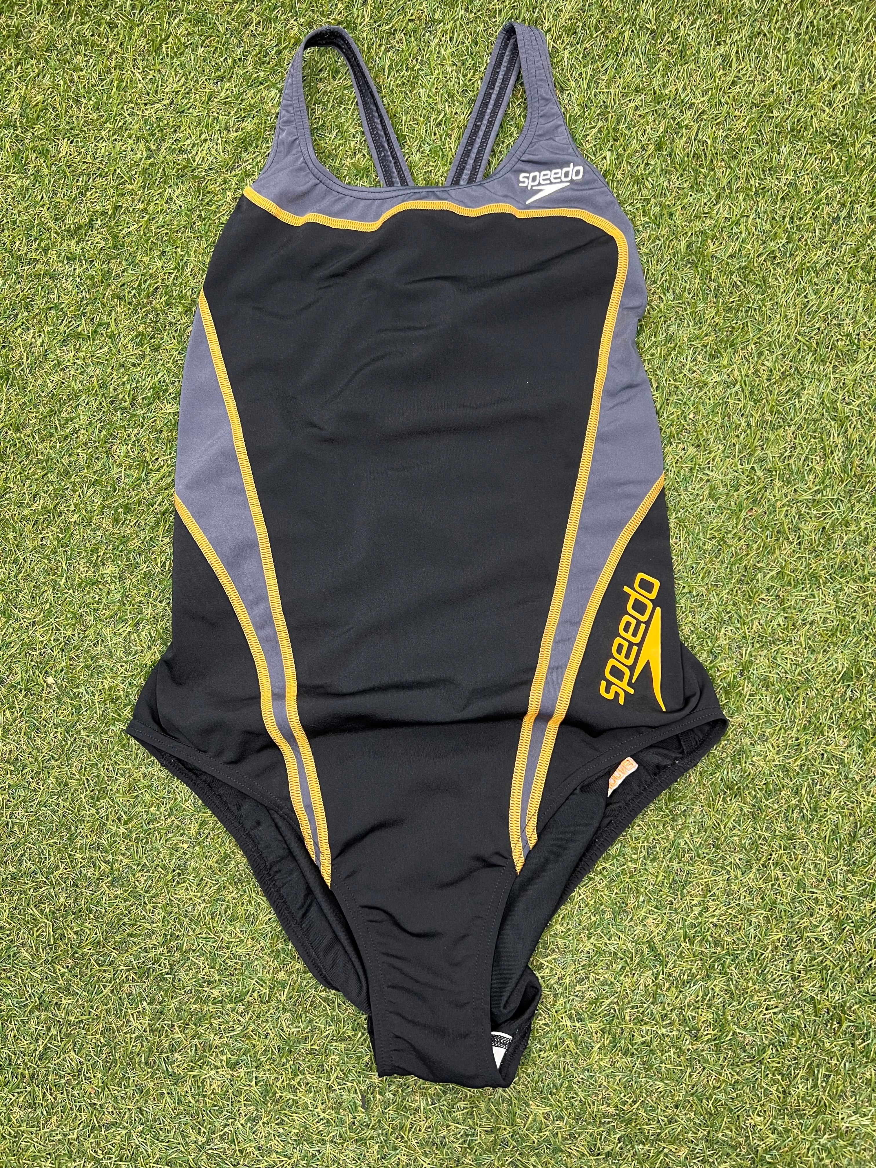 Front view of black and grey Speedo women's swimsuit with yellow detailing laid on grass