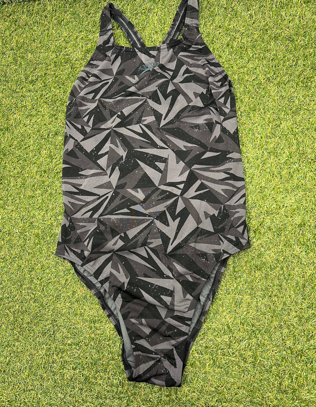 Front view of women's Speedo one-piece swimsuit with black and grey geometric pattern on grass