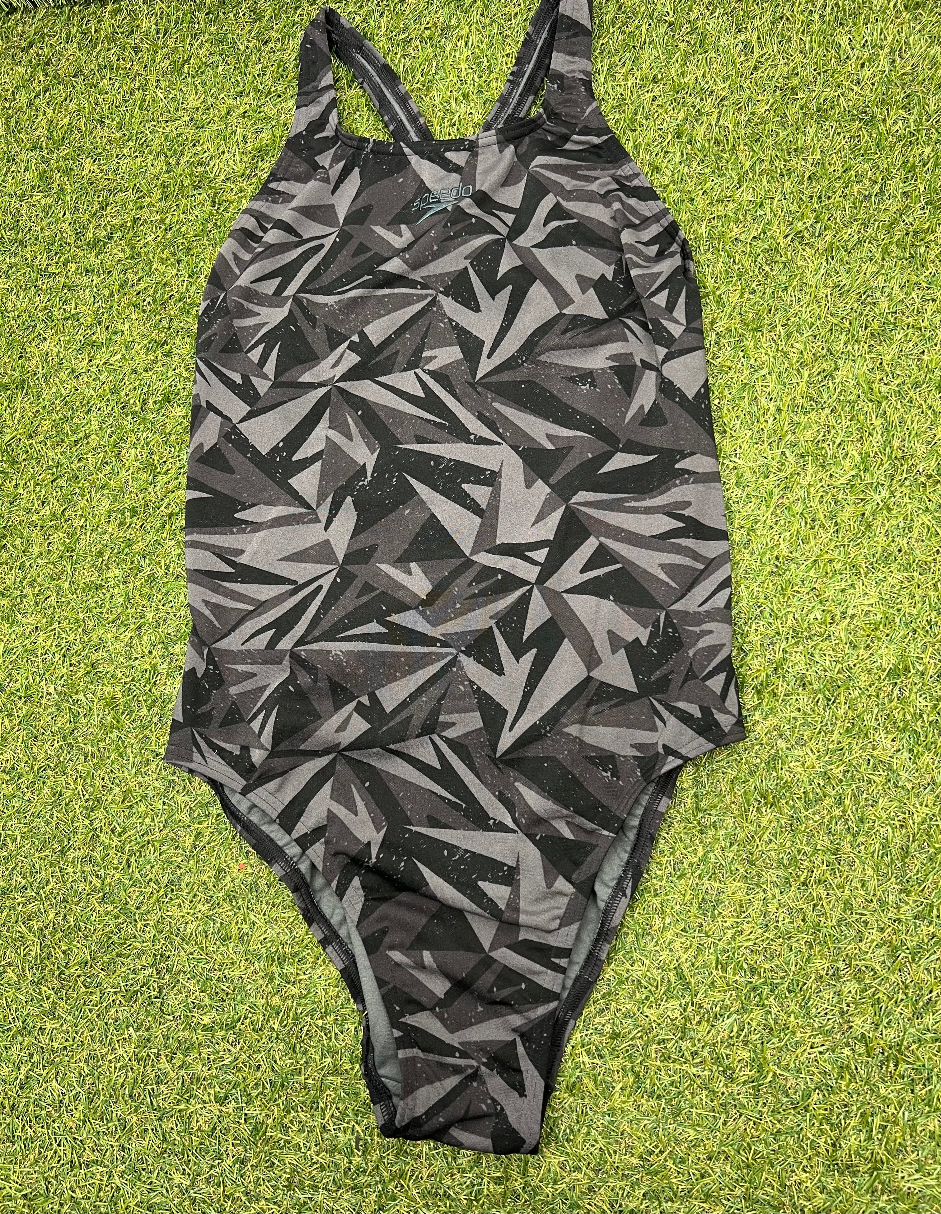 Front view of women's Speedo one-piece swimsuit with black and grey geometric pattern on grass
