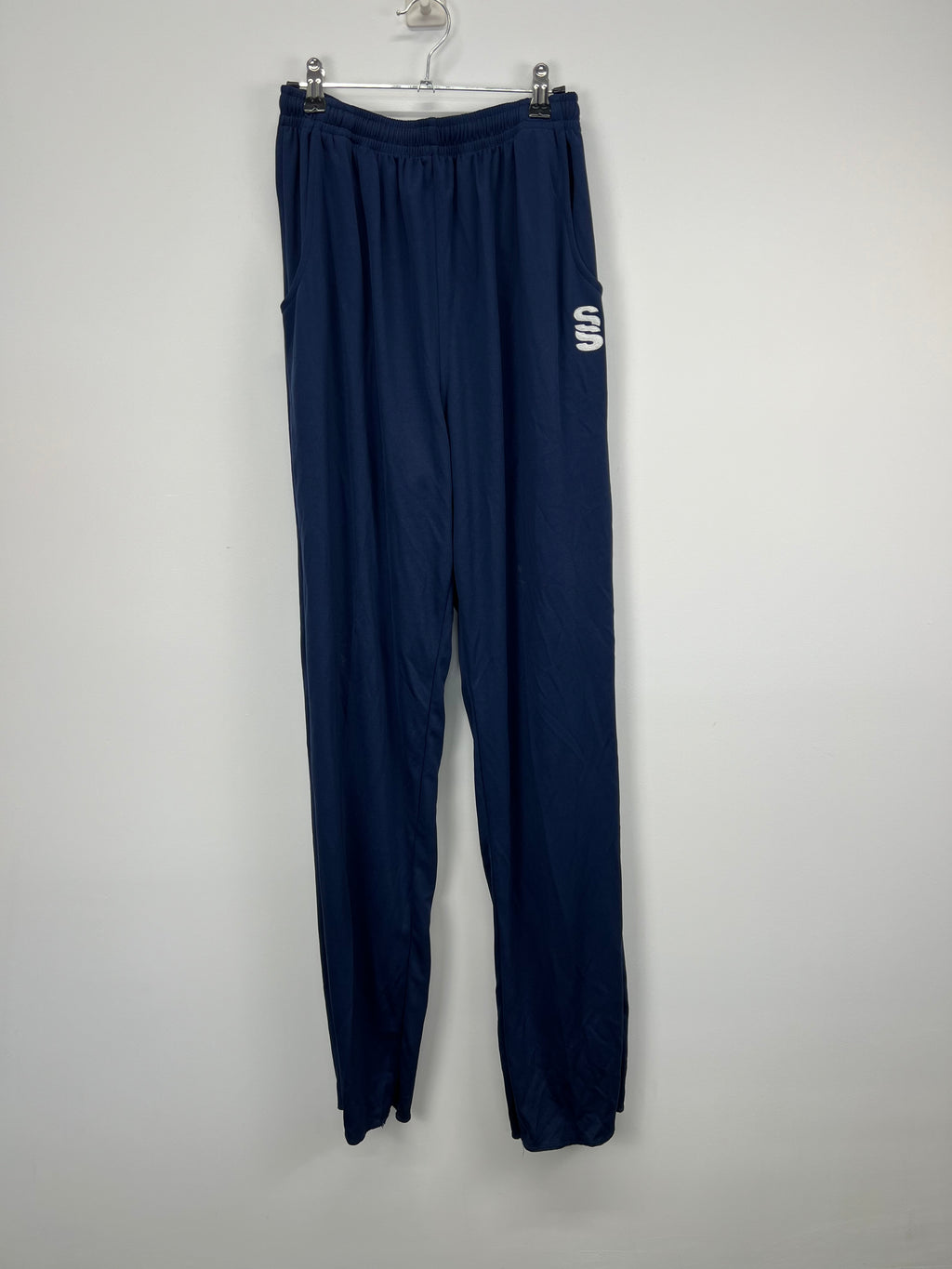 Front view of navy blue men’s Surridge cricket bottoms hanging on a hanger against a plain wall