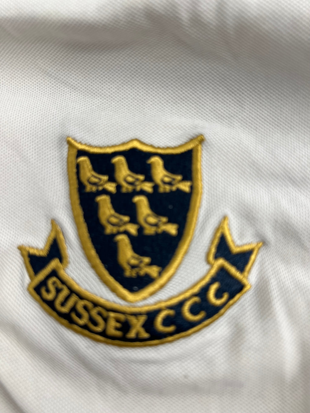 Close-up of embroidered Sussex County Cricket Club crest on white cricket jersey