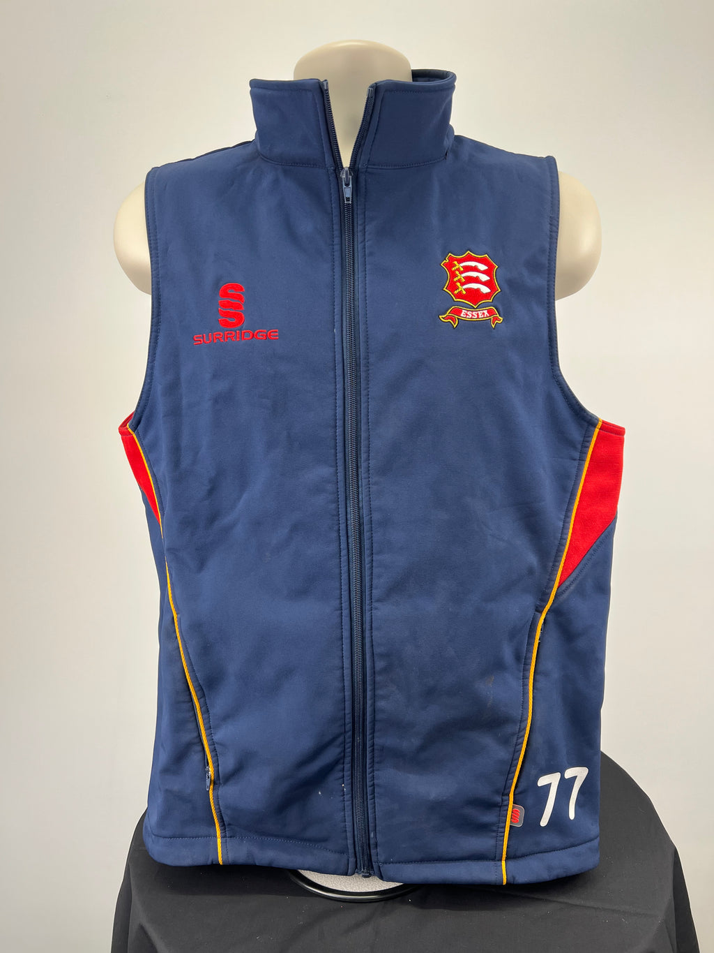 Front view of navy blue Essex County cricket gilet with red and yellow trim, Essex and Surridge logos, and number 77