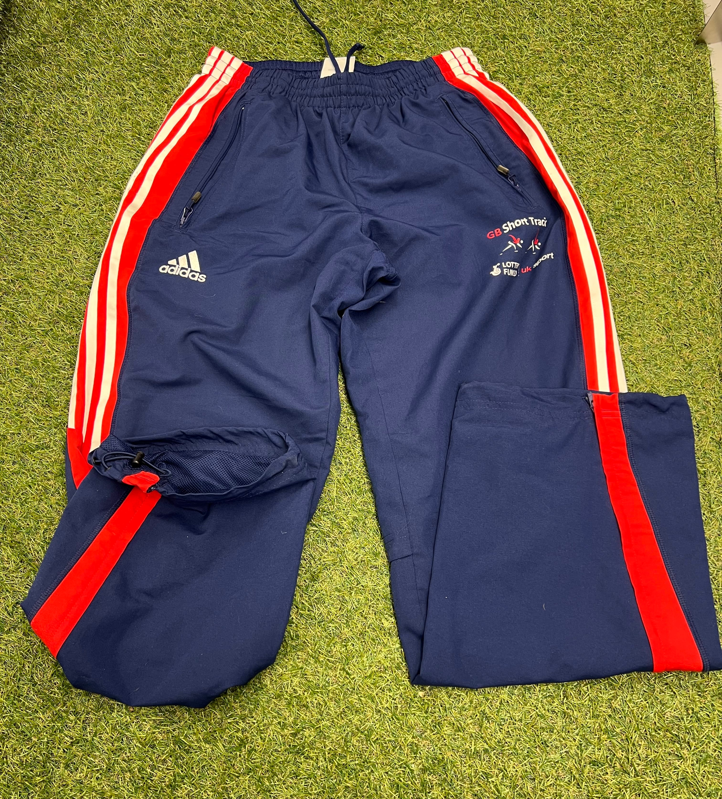 Front view of Adidas Team GB short track navy tracksuit bottoms with red and white side stripes and zippered pockets
