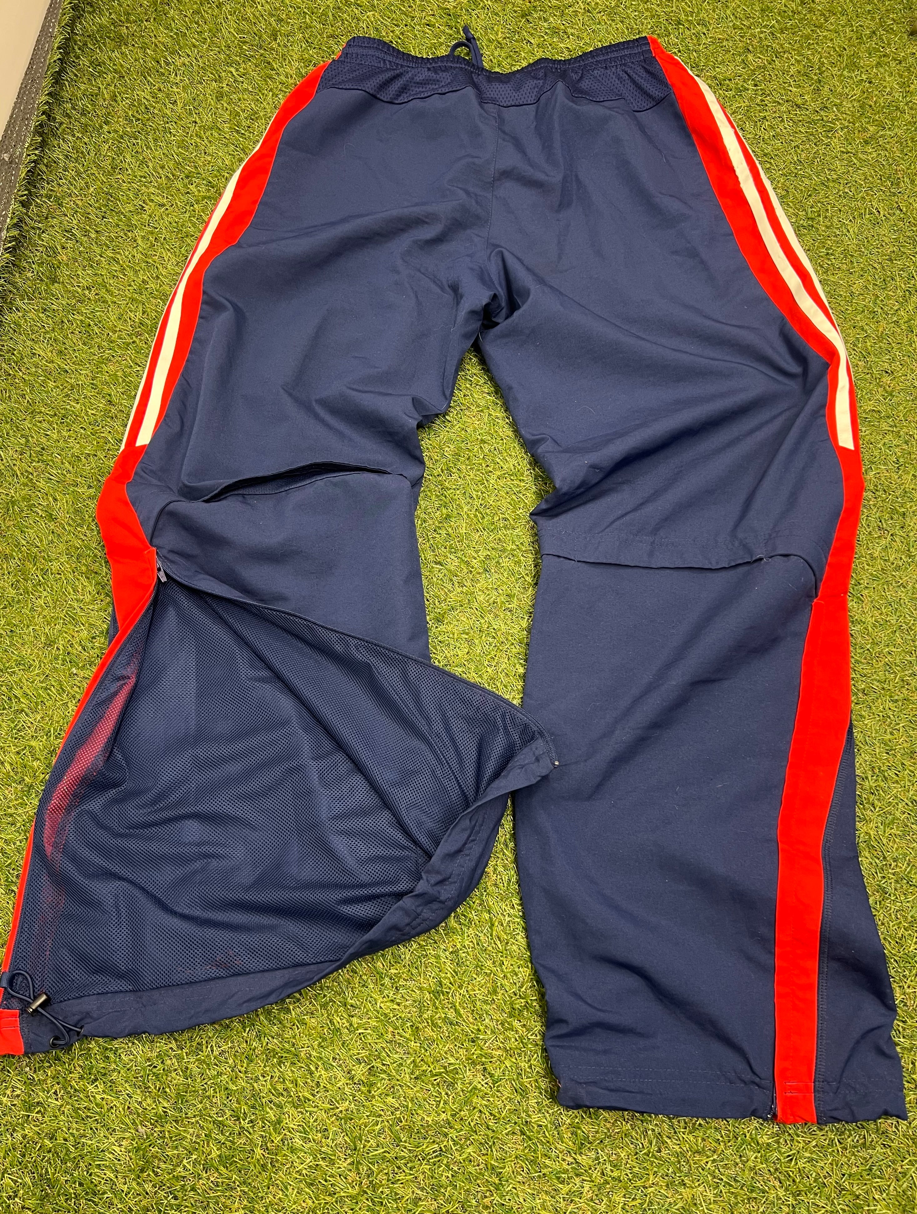 Back view of navy Adidas tracksuit bottoms with red and white stripes and open ventilation zippers at the bottom