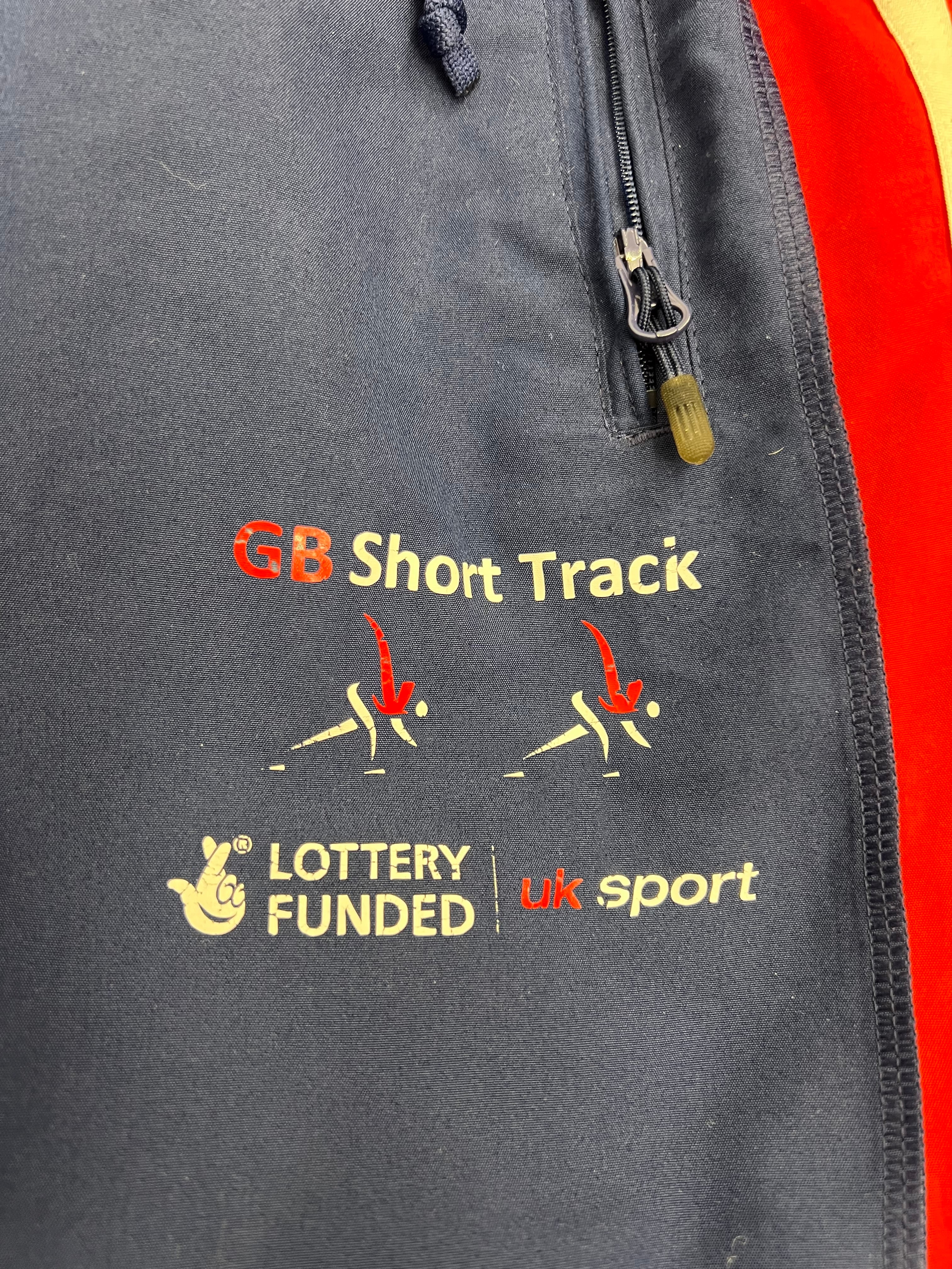 Close-up of GB Short Track and Lottery Funded UK Sport logos printed on navy Adidas tracksuit bottoms