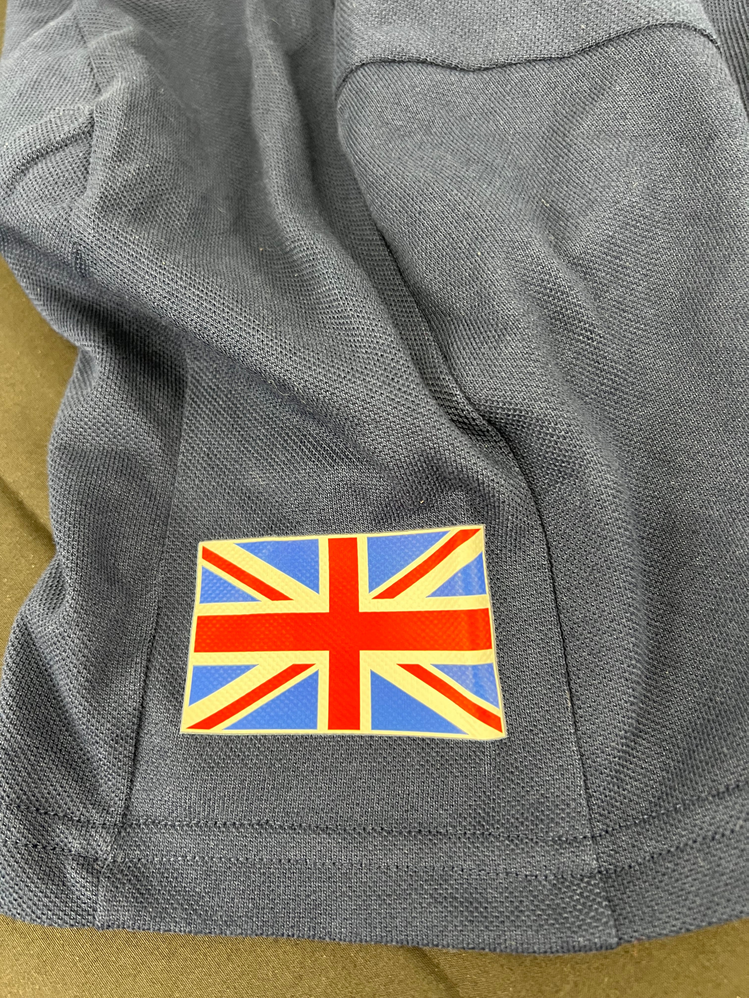 Close-up of the UK flag patch on the sleeve of the indigo Adidas polo shirt