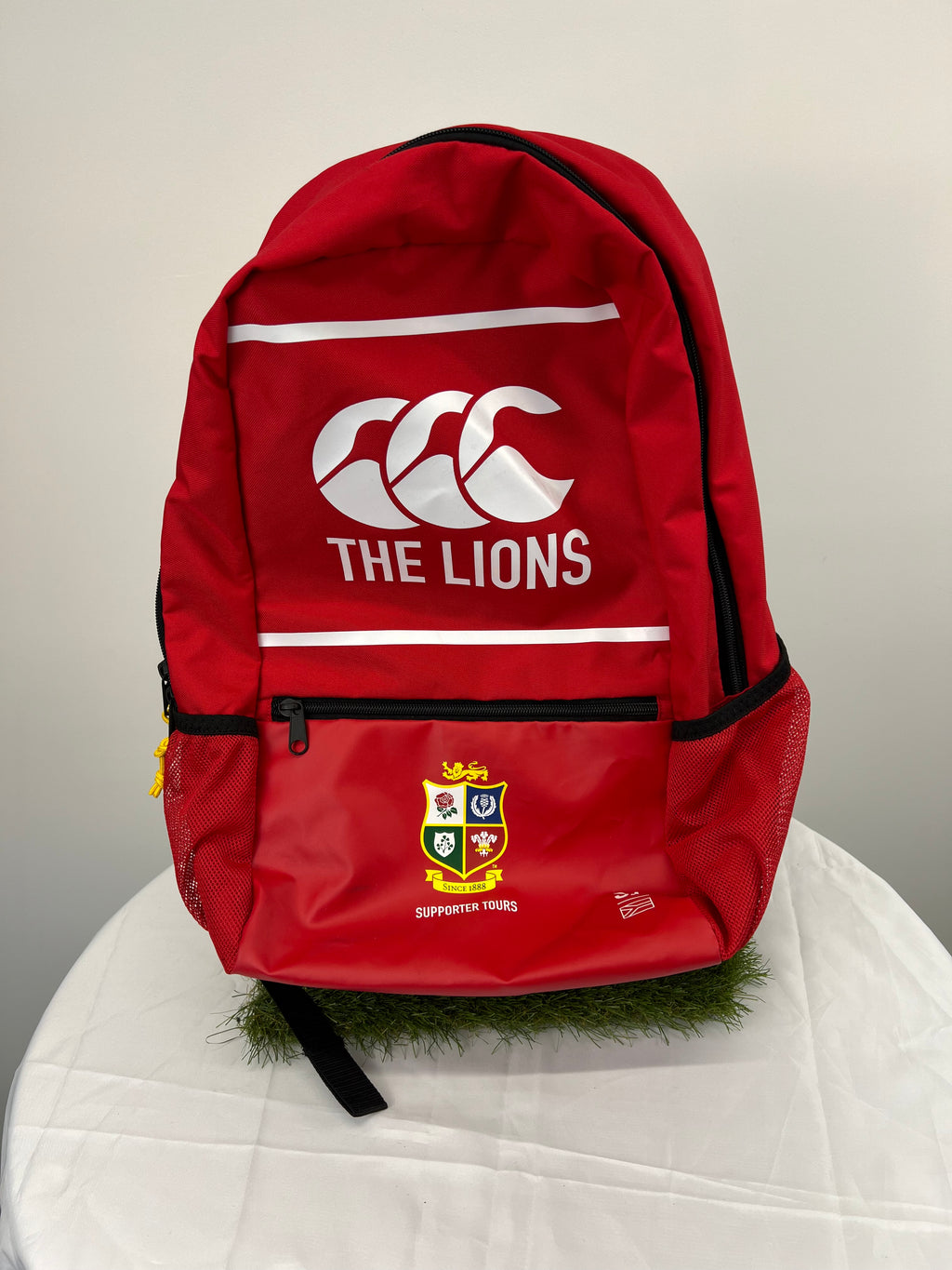 Front view of red rugby supporters backpack with The Lions and crest logos on white table