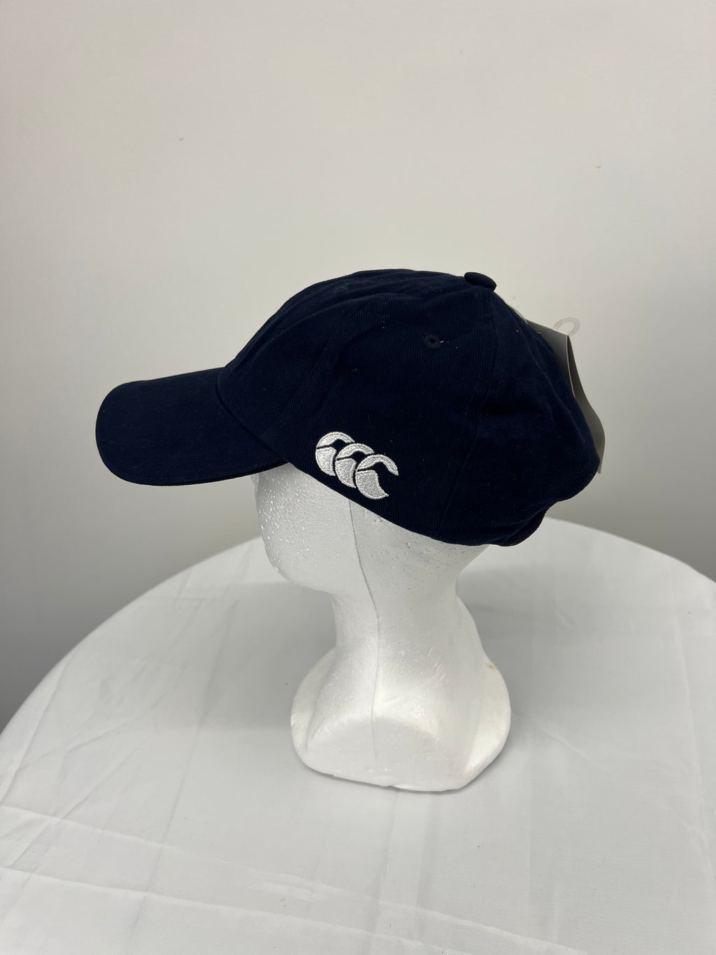 Side view of navy blue Canterbury cap with white embroidered Canterbury logo on a white mannequin head