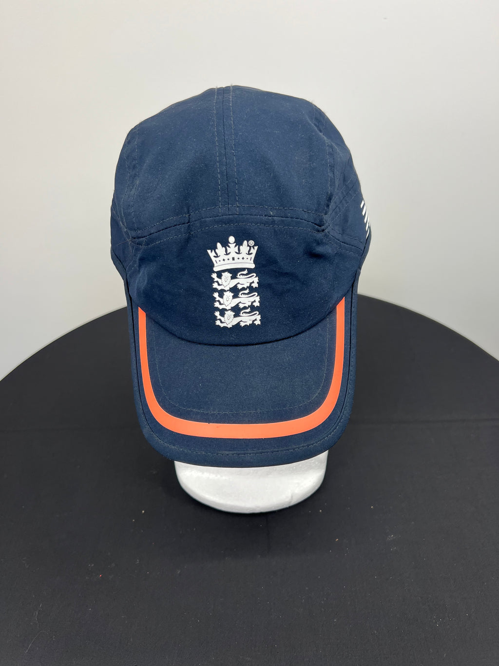 Front view of New Balance navy cricket baseball cap with white three lions emblem and orange trim on visor