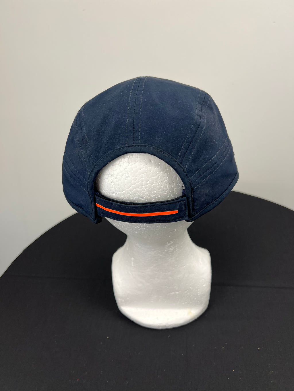 Back view of navy New Balance cricket baseball cap with adjustable strap featuring orange stripe