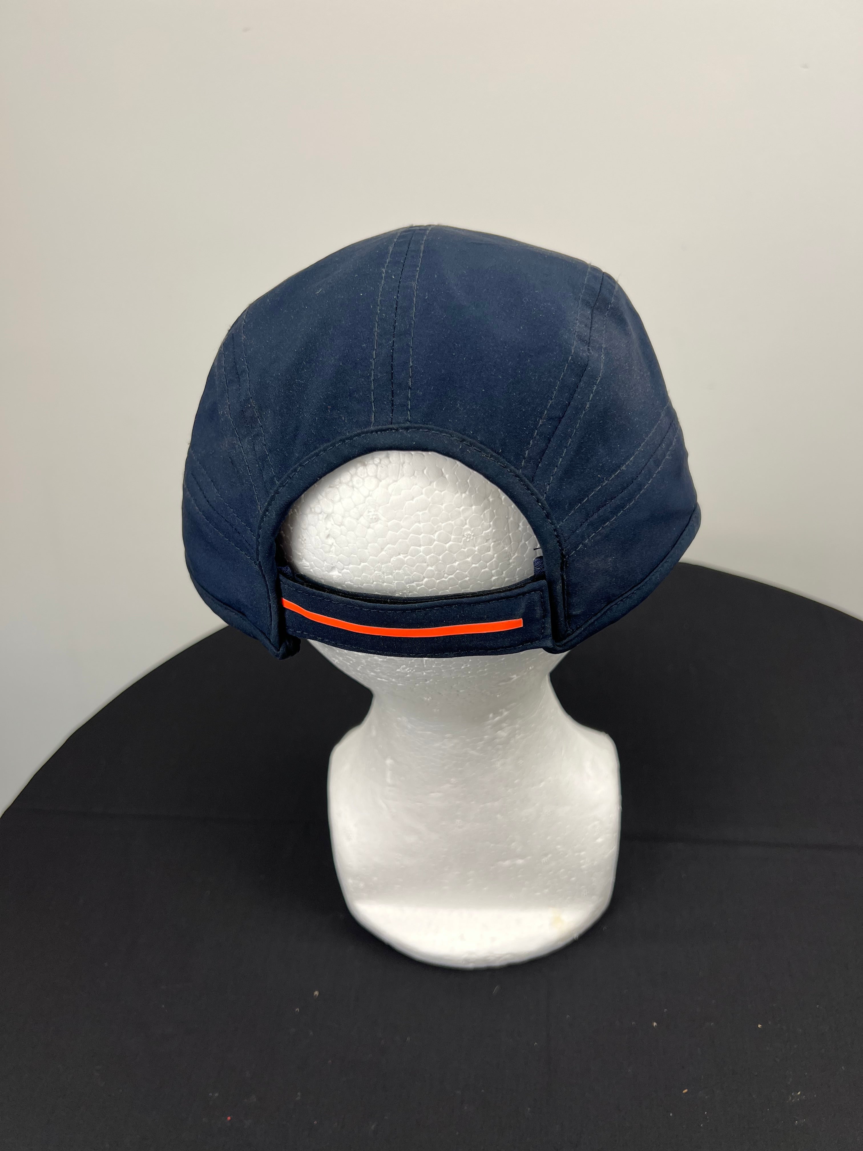 Back view of navy New Balance cricket baseball cap with adjustable strap featuring orange stripe