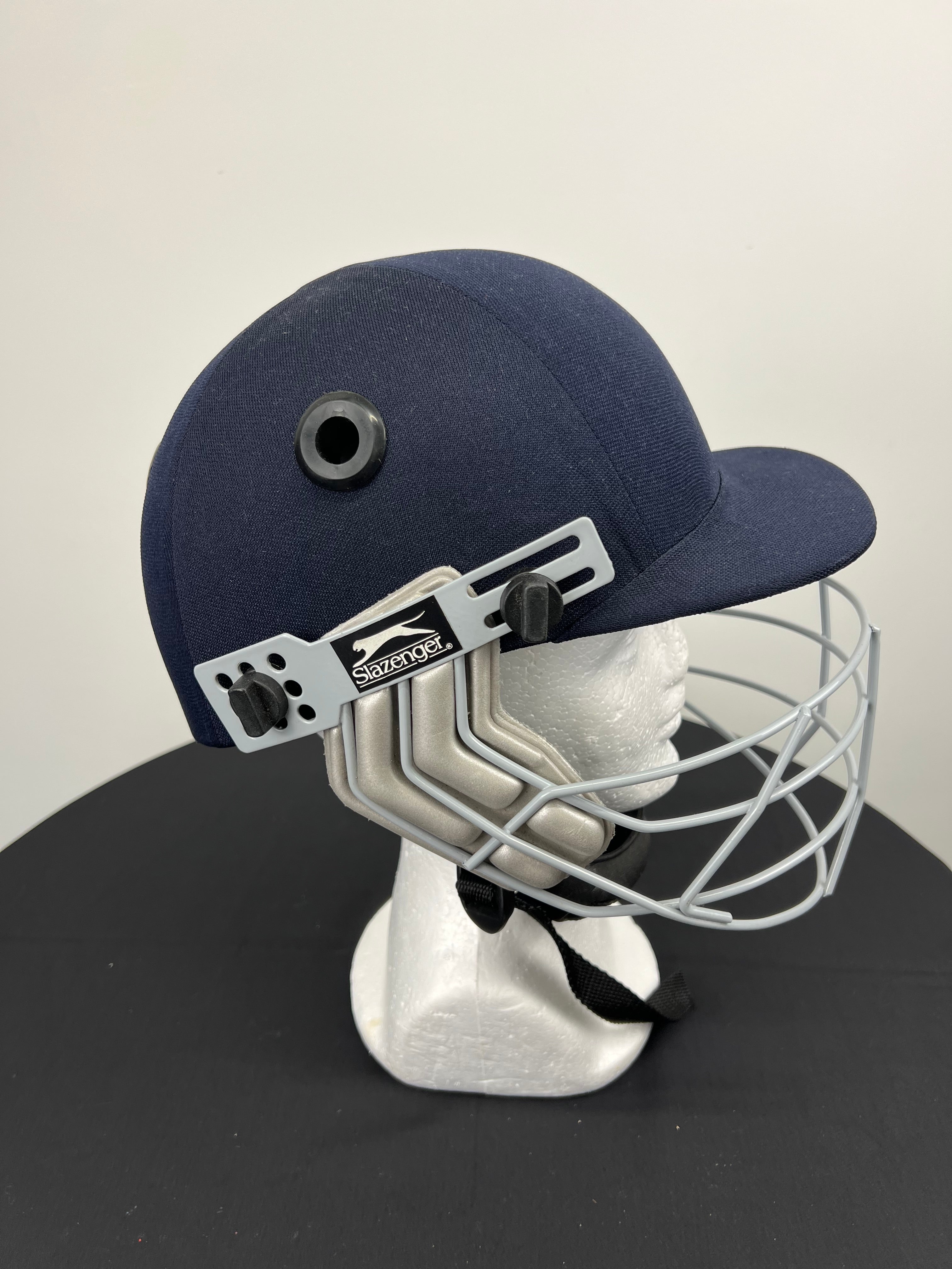 Side view of navy blue Slazenger cricket helmet showing adjustable straps and protective face guard
