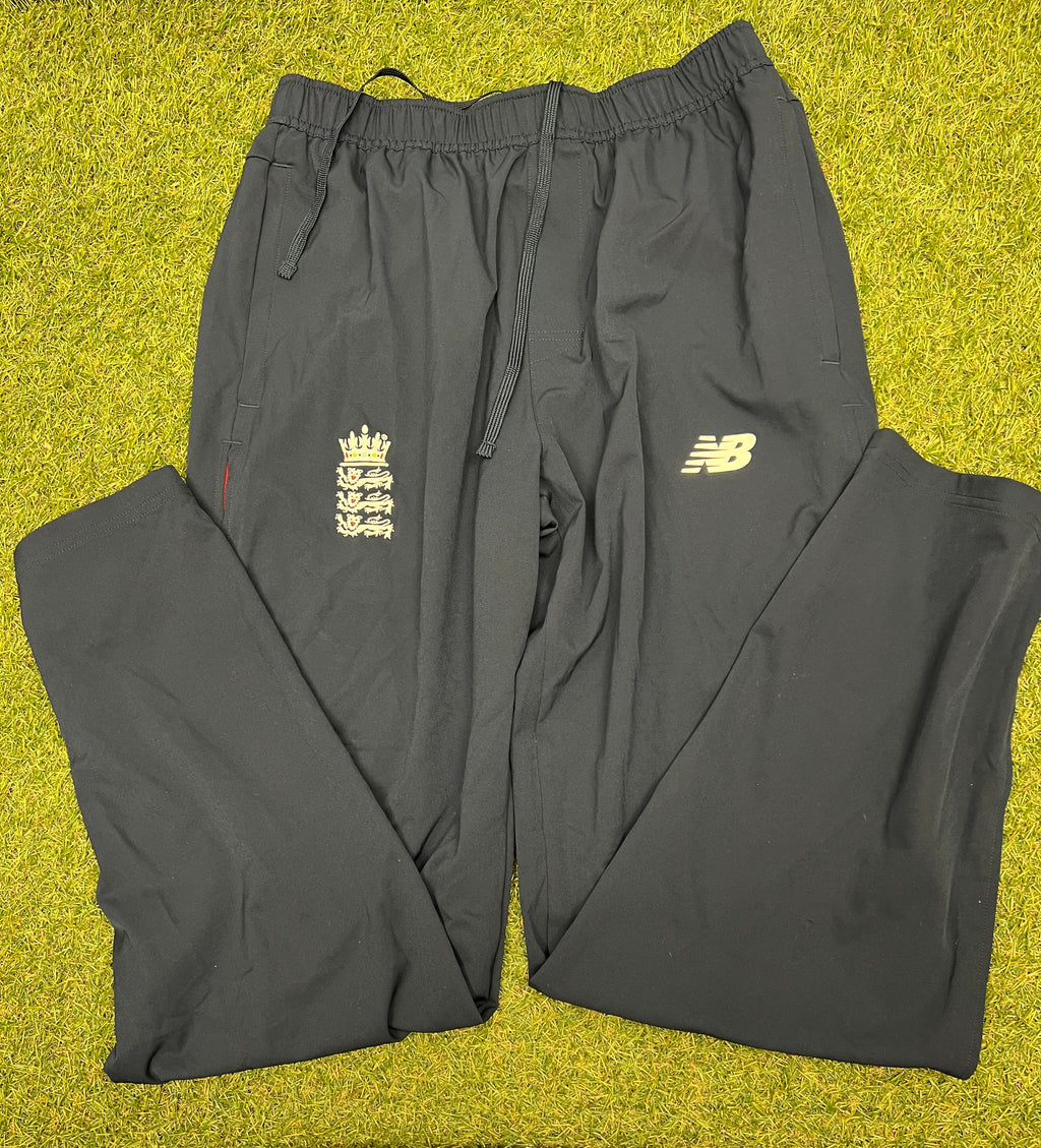 Front view of black Men's New Balance England cricket tracksuit bottoms with elastic waistband and drawstring on grass
