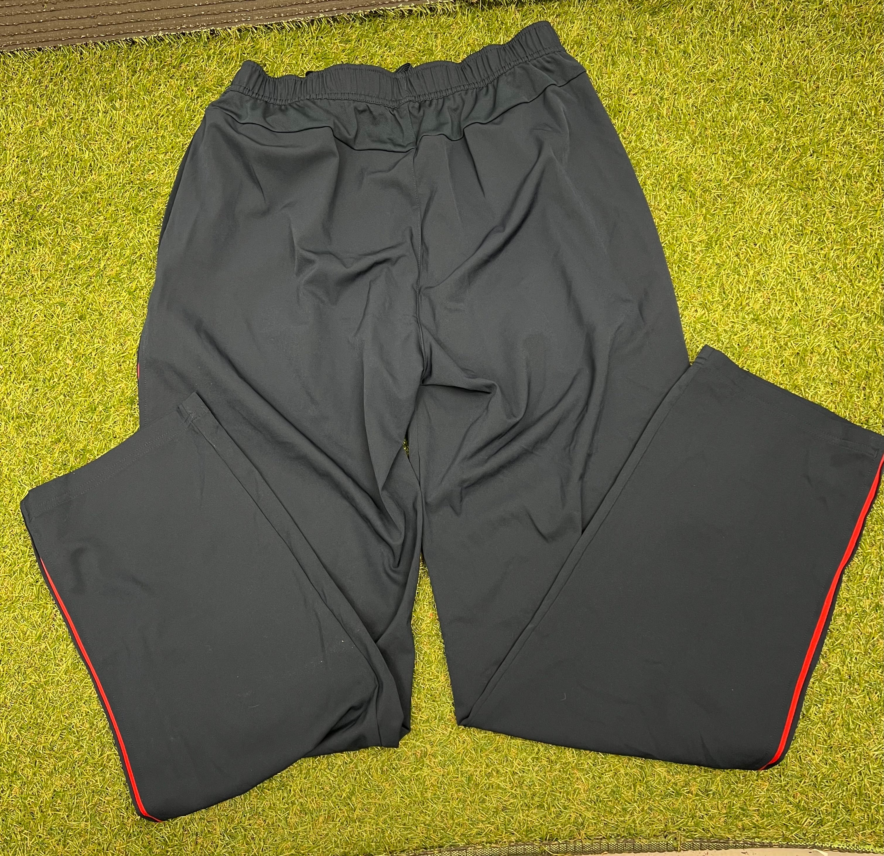 Back view of black cricket tracksuit bottoms with red side stripes laid on grass surface