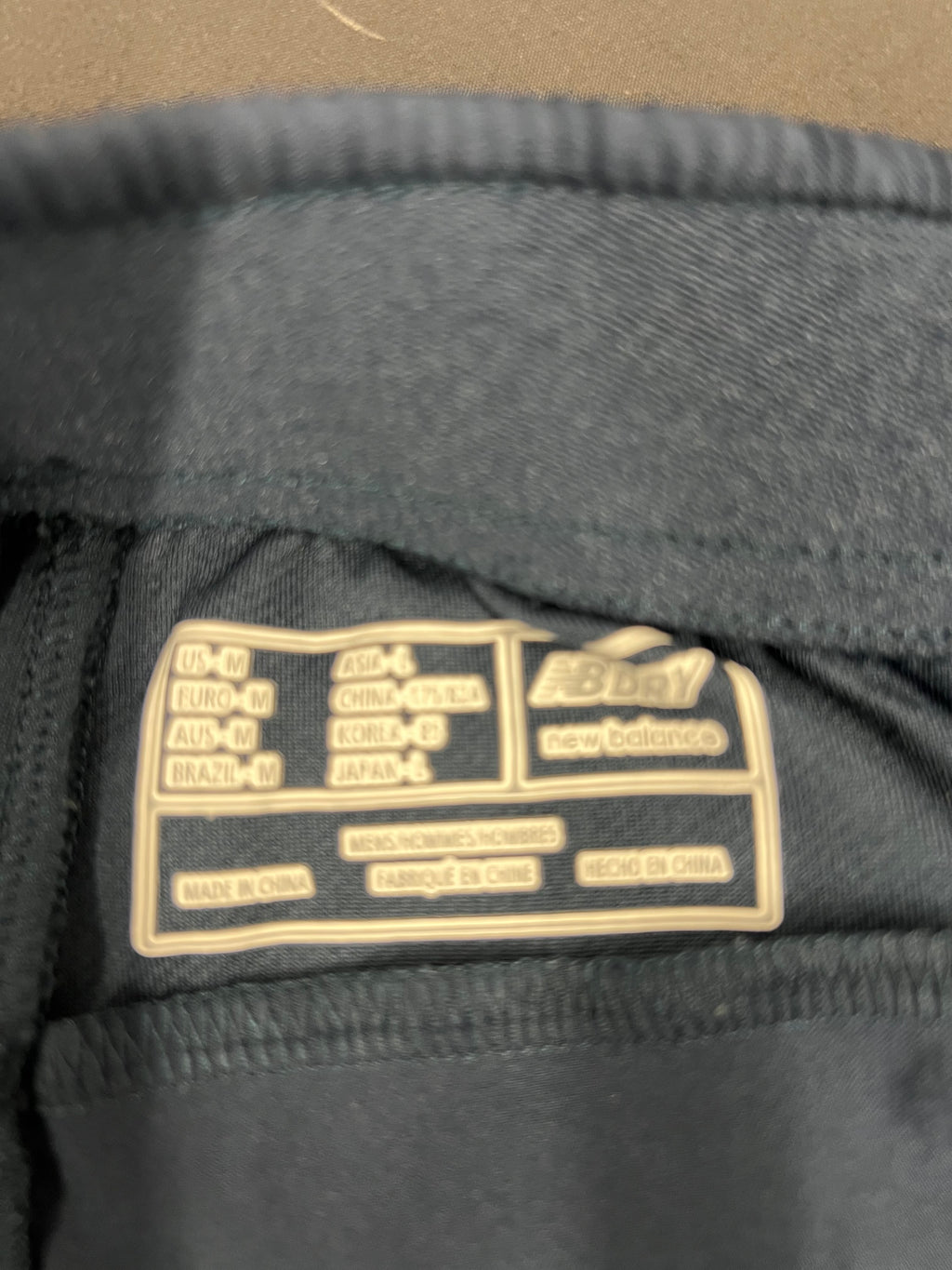 Close-up of size and care label inside New Balance England cricket tracksuit bottoms showing medium size and NB Dry logo