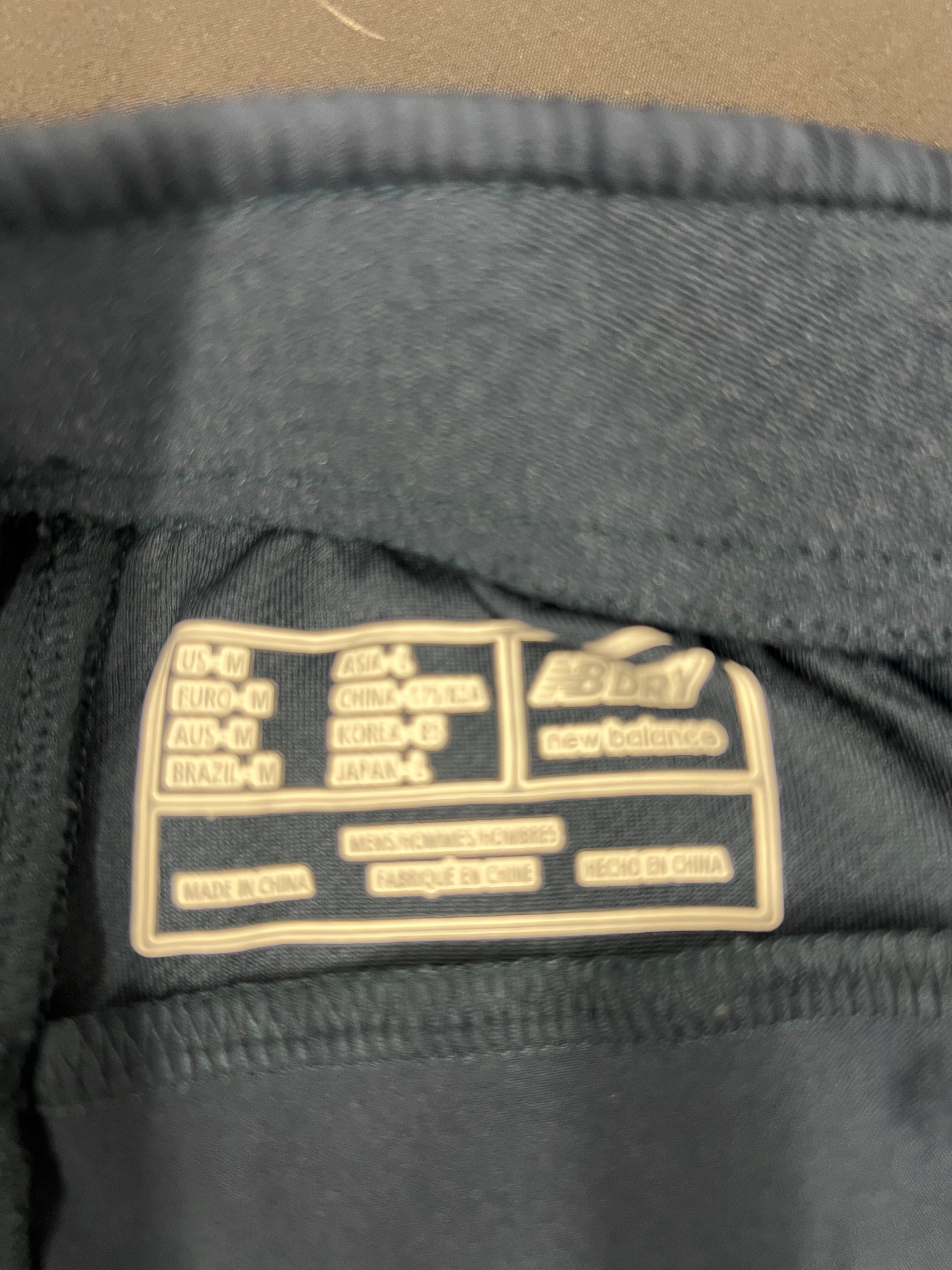 Close-up of size and care label inside New Balance England cricket tracksuit bottoms showing medium size and NB Dry logo