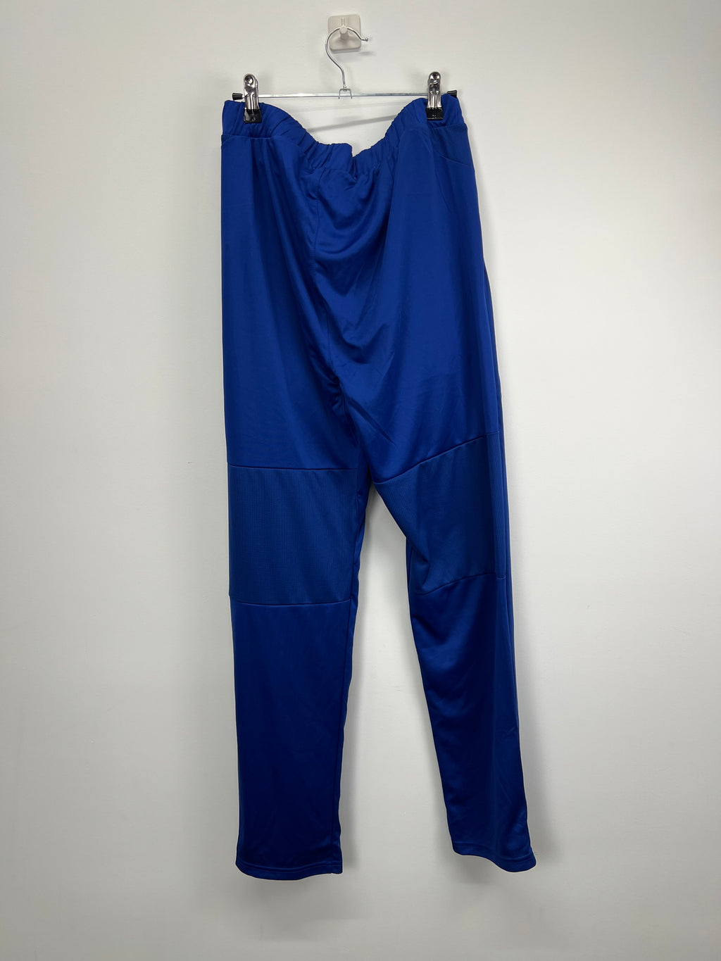 Back view of men’s royal blue Castore England cricket tracksuit bottoms hanging on a hanger