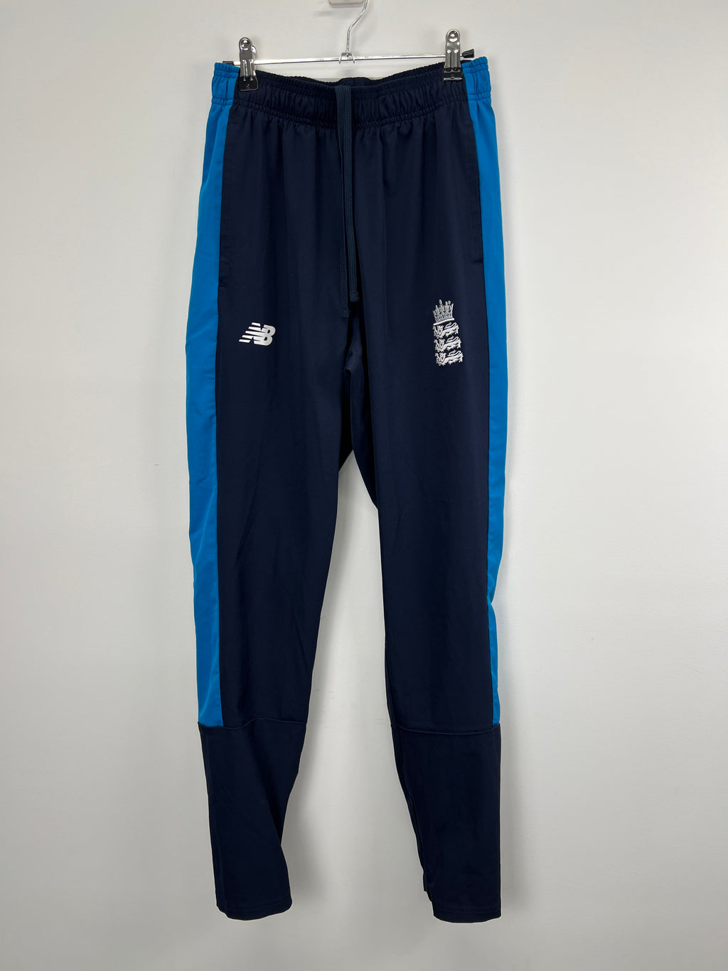 Front view of Men’s New Balance England cricket tracksuit trousers in navy with blue side panels on hanger